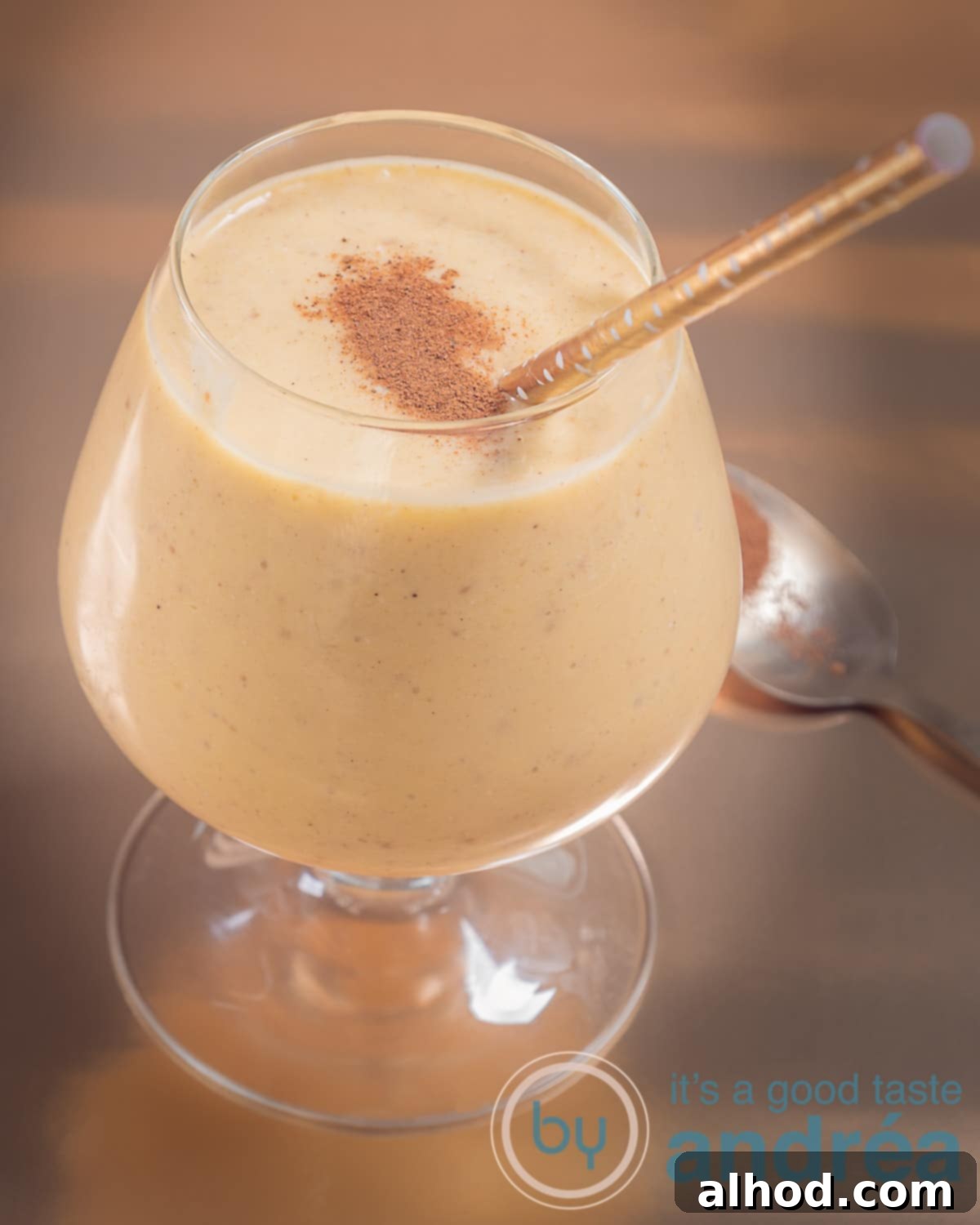 Tropical Mango Date Coconut Dream 3 A photo of a glass with a tropical mango coconut smoothie. Some cinnamon on top and a golden straw and background.