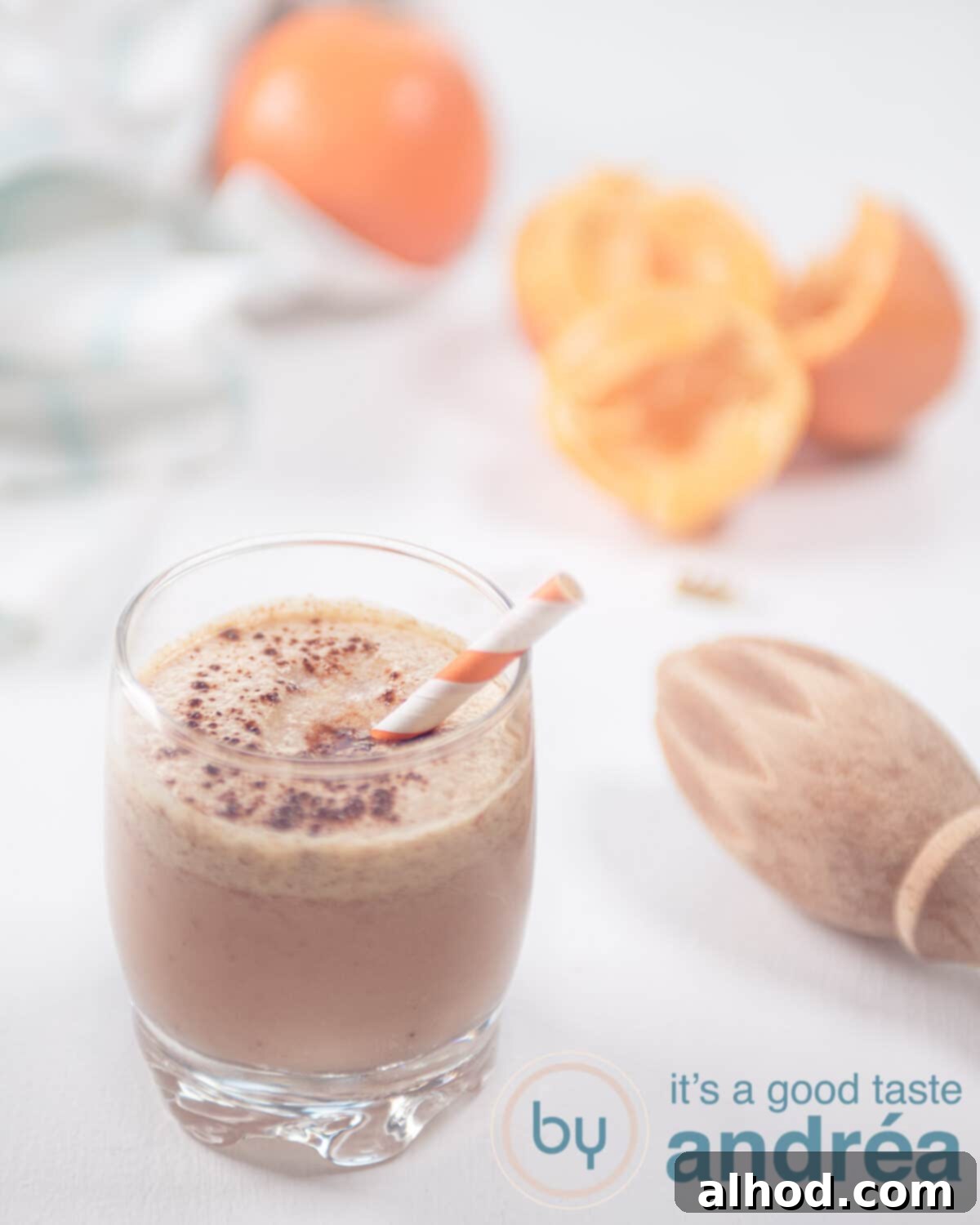 Dairy Free Tangerine Smoothie 2 A vibrant tangerine and cranberry smoothie in a glass, with fresh tangerines and juiced halves in the background, set against a light, inviting backdrop.
