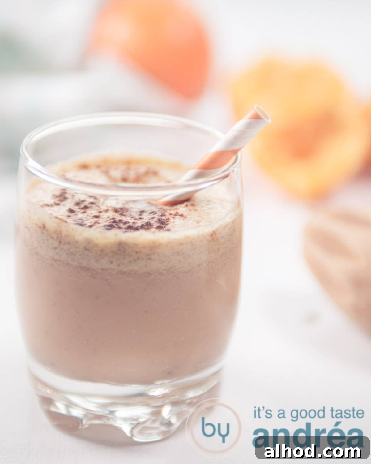Dairy Free Tangerine Smoothie 5 A beautifully presented tangerine smoothie, garnished with a sprinkle of cocoa, with fresh tangerines in the soft-focused background, emphasizing its creamy texture and vibrant color.