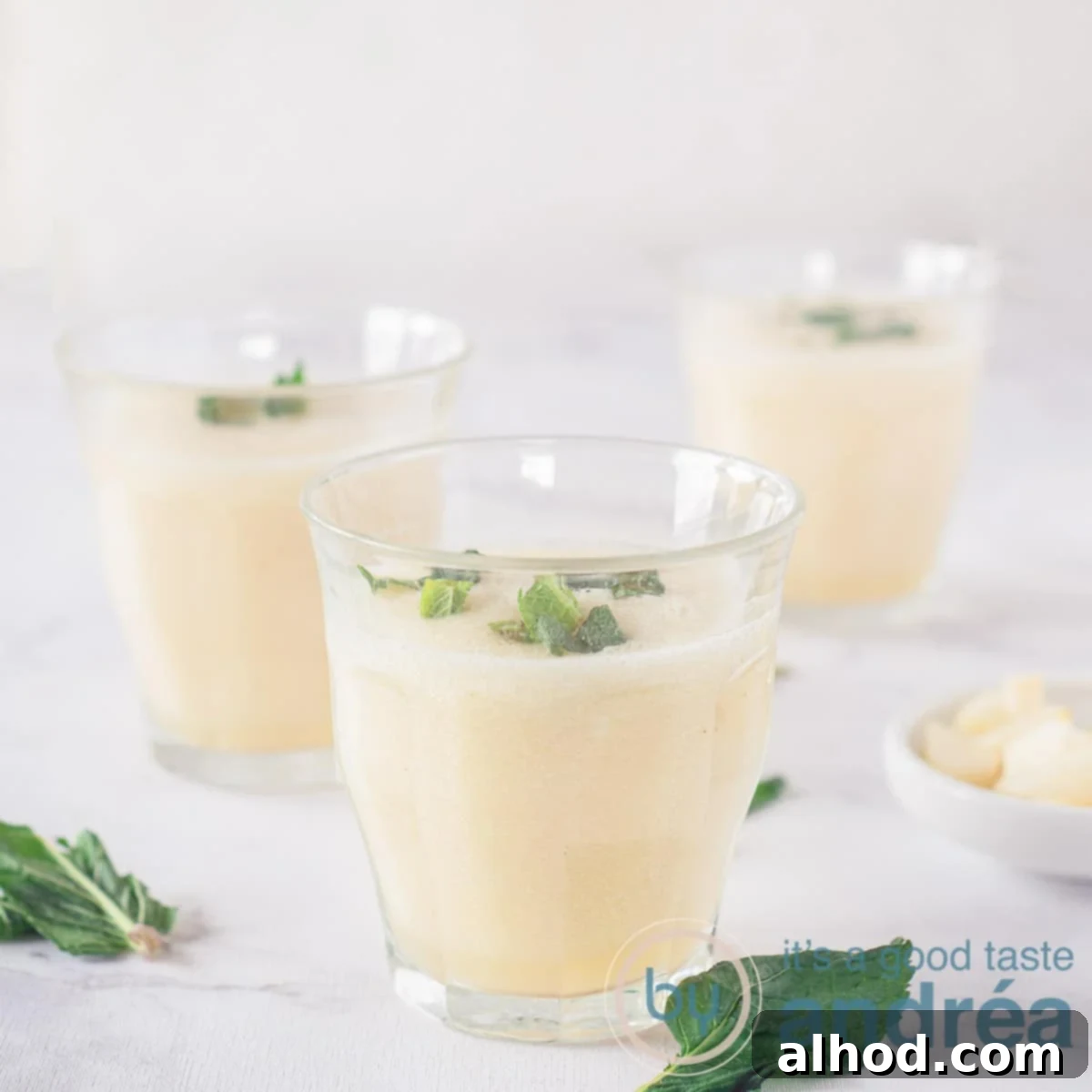 A square photo with three glasses filled with a vanilla, pear and coconut water smoothie. With fresh mint, which is also around it. A white background