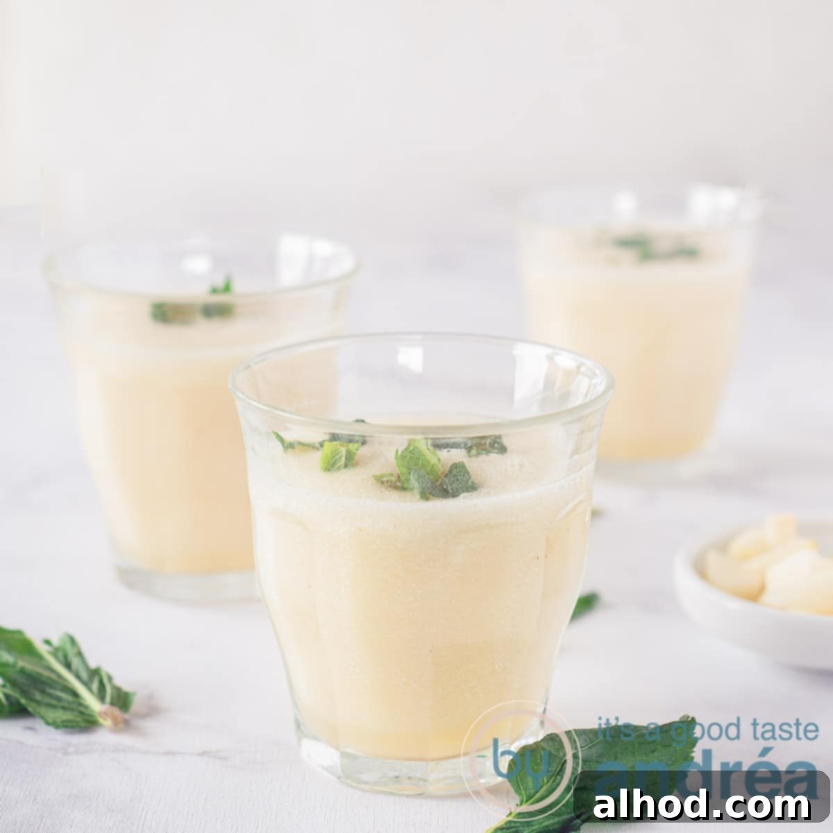 6 Coconut Smoothie Recipes 2 Three glasses filled with a creamy vanilla, pear, and coconut water smoothie, garnished with fresh mint. The glasses are set against a clean white background.
