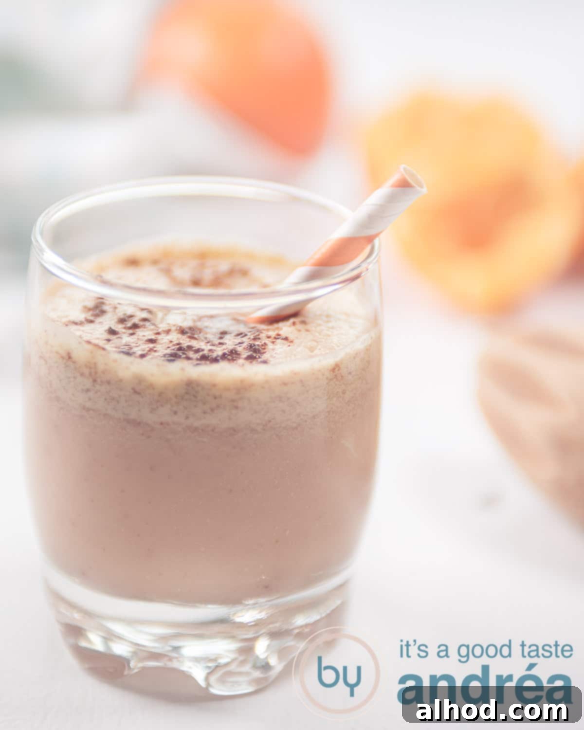 6 Coconut Smoothie Recipes 4 A vibrant tangerine smoothie in a glass, with fresh tangerines and some squeezed juice in the soft-focus background.