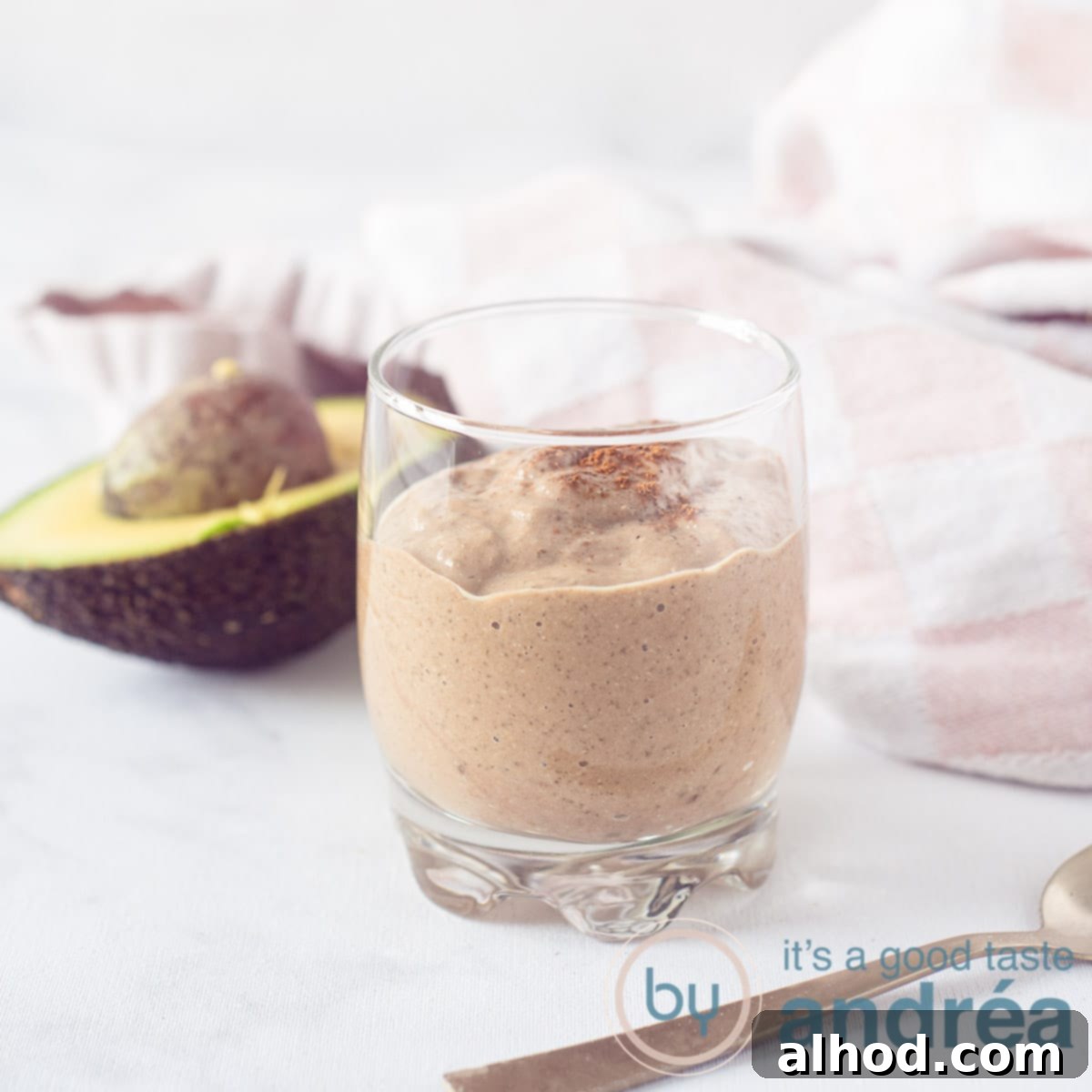 6 Coconut Smoothie Recipes 5 A glass of rich chocolate coconut smoothie with an avocado and a pink and white tea towel blurred in the background, creating a cozy atmosphere.