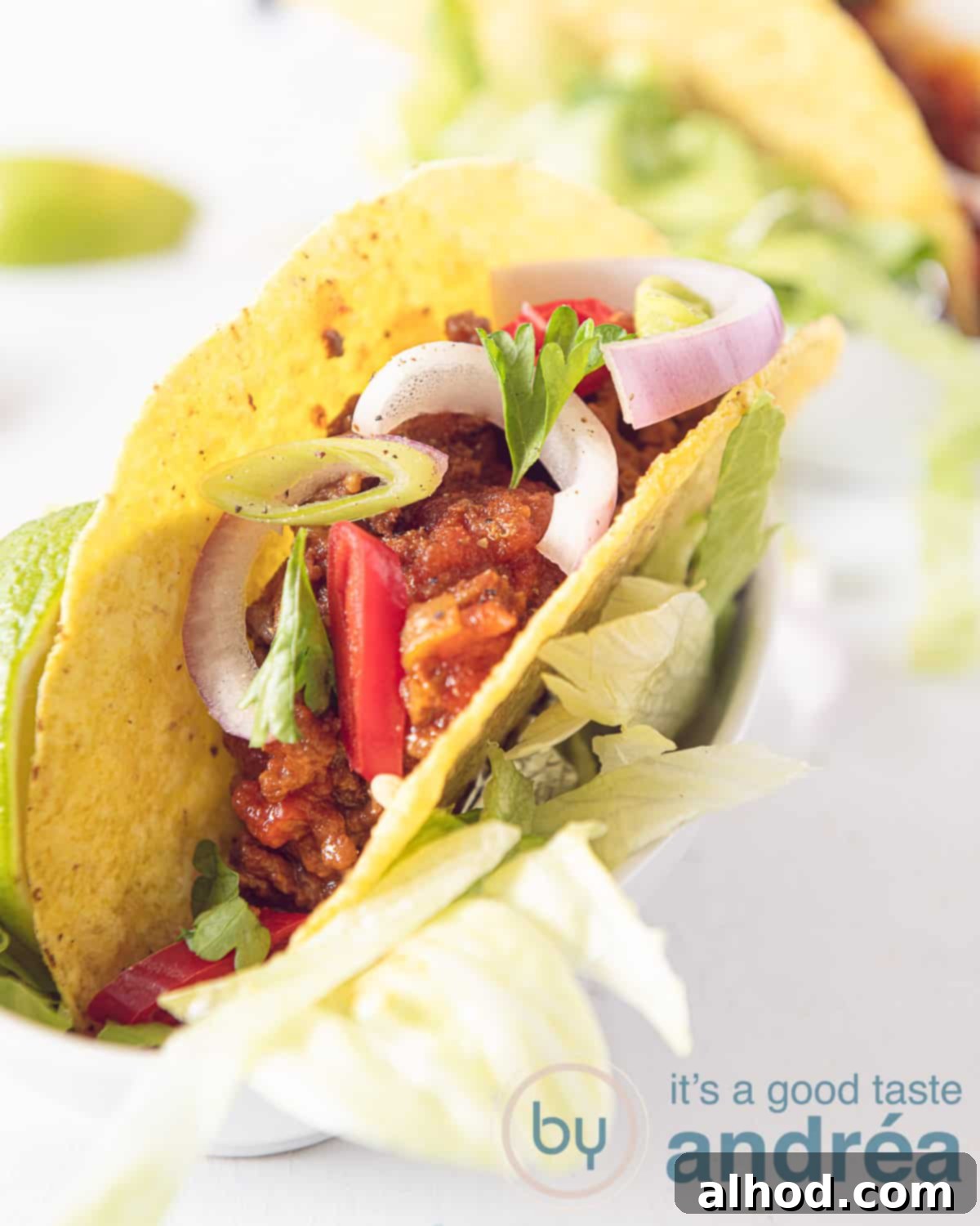 Effortless All-Meat Slow Cooker Chili 2 A vibrant taco filled with slow cooker no-bean chili, topped with fresh onions, diced tomatoes, and crisp lettuce, set against a clean white background.