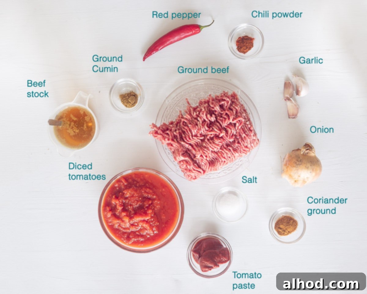 Effortless All-Meat Slow Cooker Chili 3 A collection of fresh ingredients for slow cooker no-bean chili, including ground beef, diced tomatoes, beef stock, onions, garlic, and various spices, all neatly arranged on a white background.