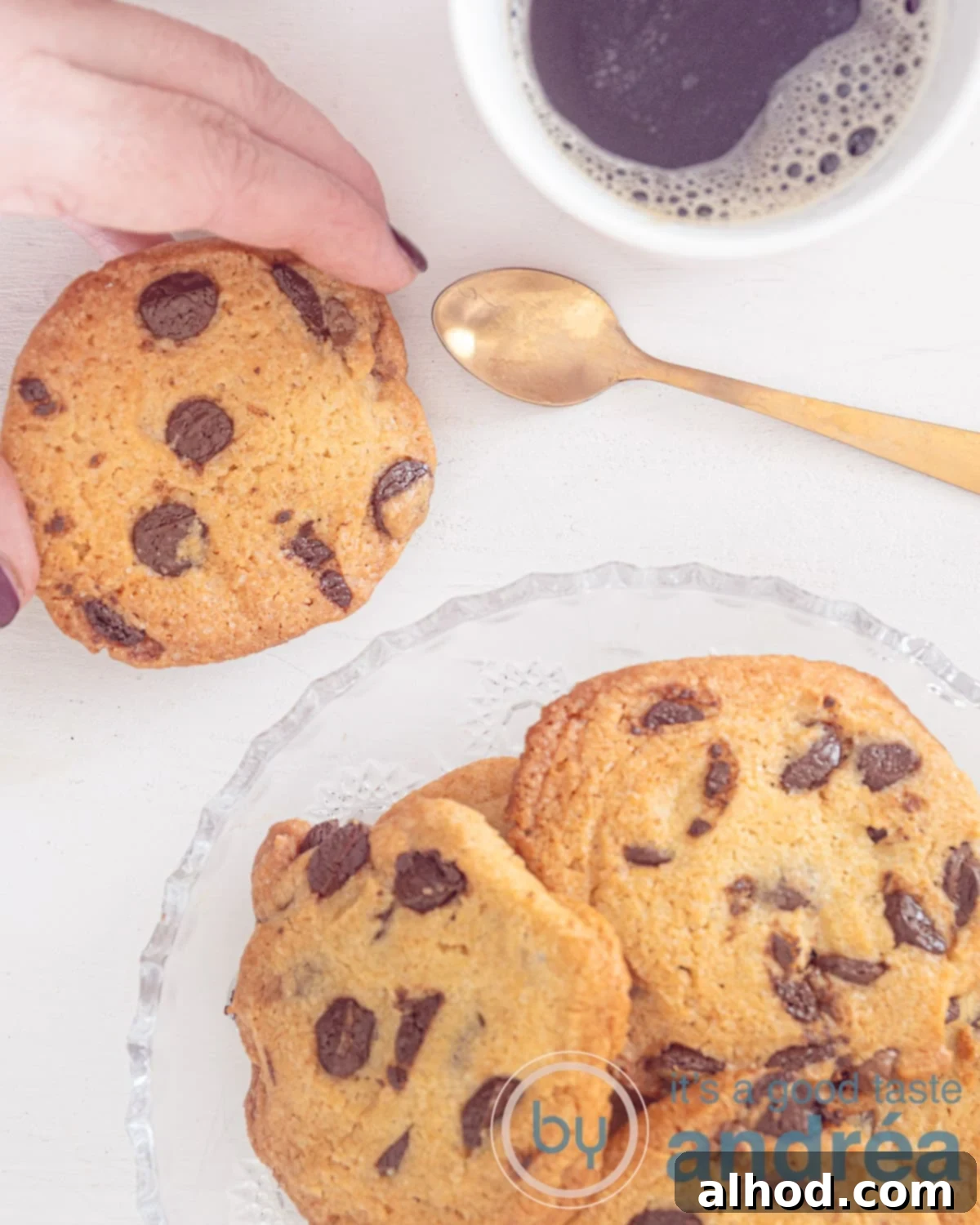 Your Personal Small Batch Chocolate Chip Treat 2 A photo from above of a white background. At the bottom right a bowl with cookies. At the top left a chocolate chip cookie that is being grabbed. At the top right a golden spoon and a mug with coffee.