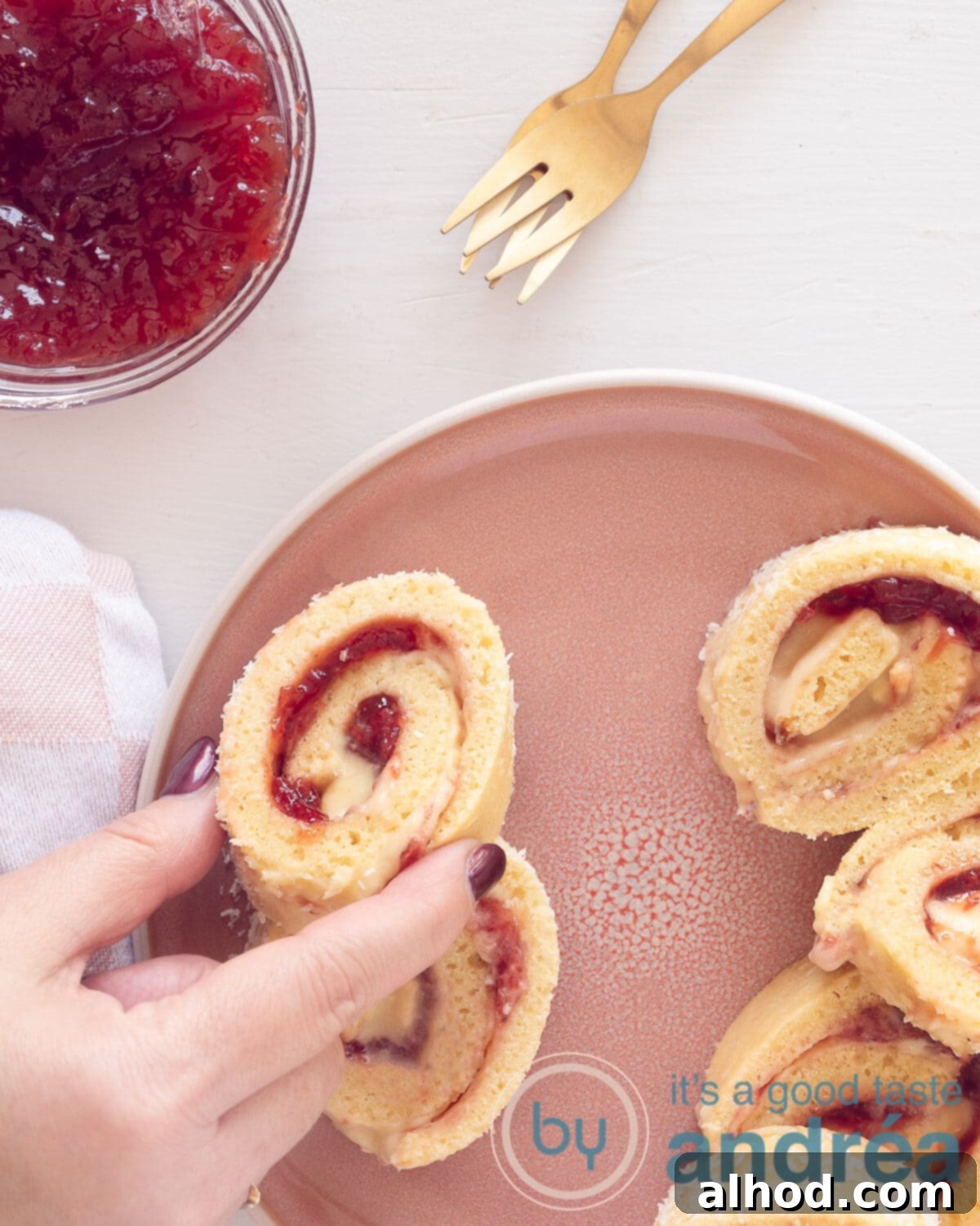Strawberry Swiss Roll 2 A photo from above with rolls of cake filled with strawberry jam and cream. On the top left a bowl with jam and two golden forks