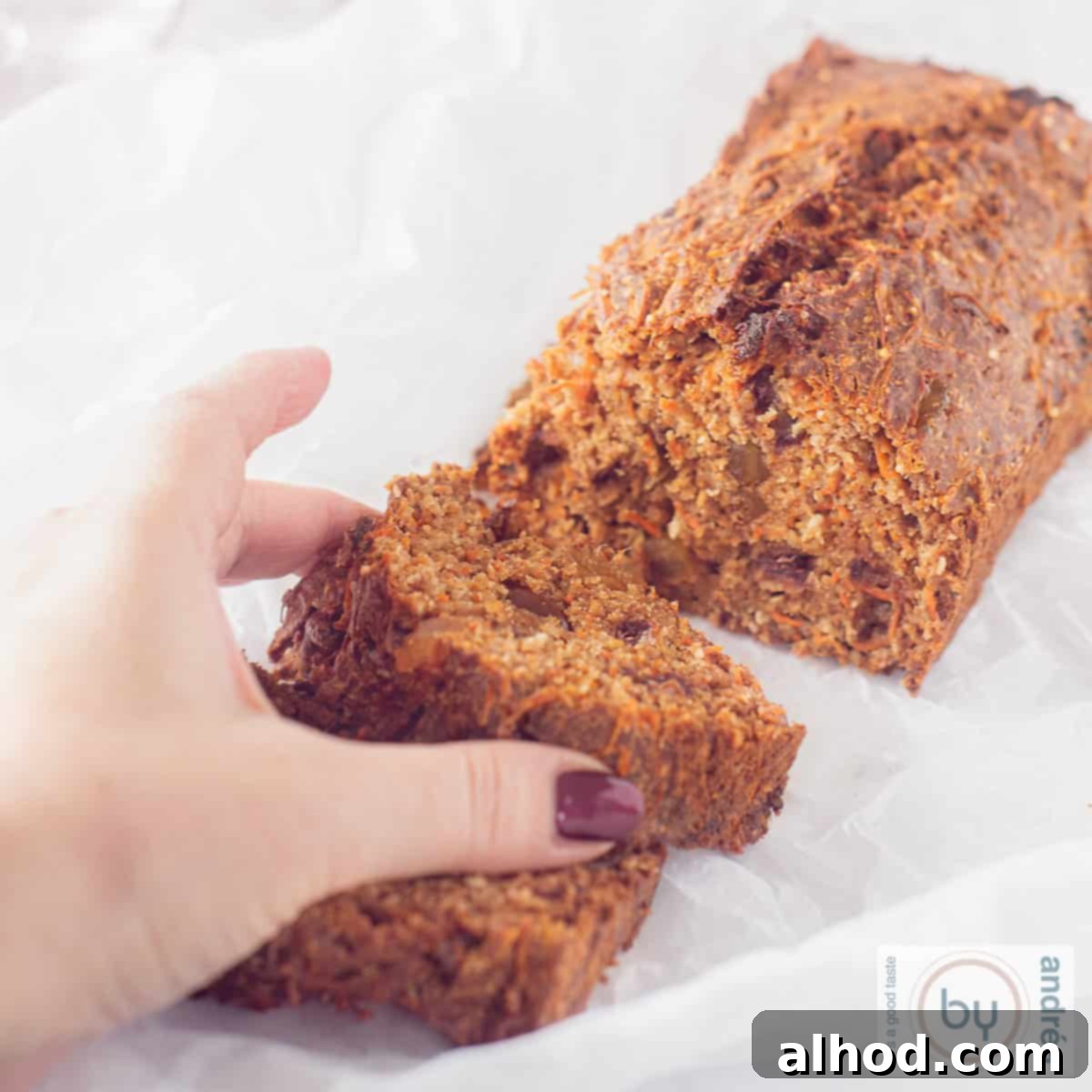 Wholesome Sugar-Free Carrot Cake Loaf 3 A square photo of a sugar-free carrot cake loaf with two slices cut, showing its moist texture and a hand reaching for a slice.