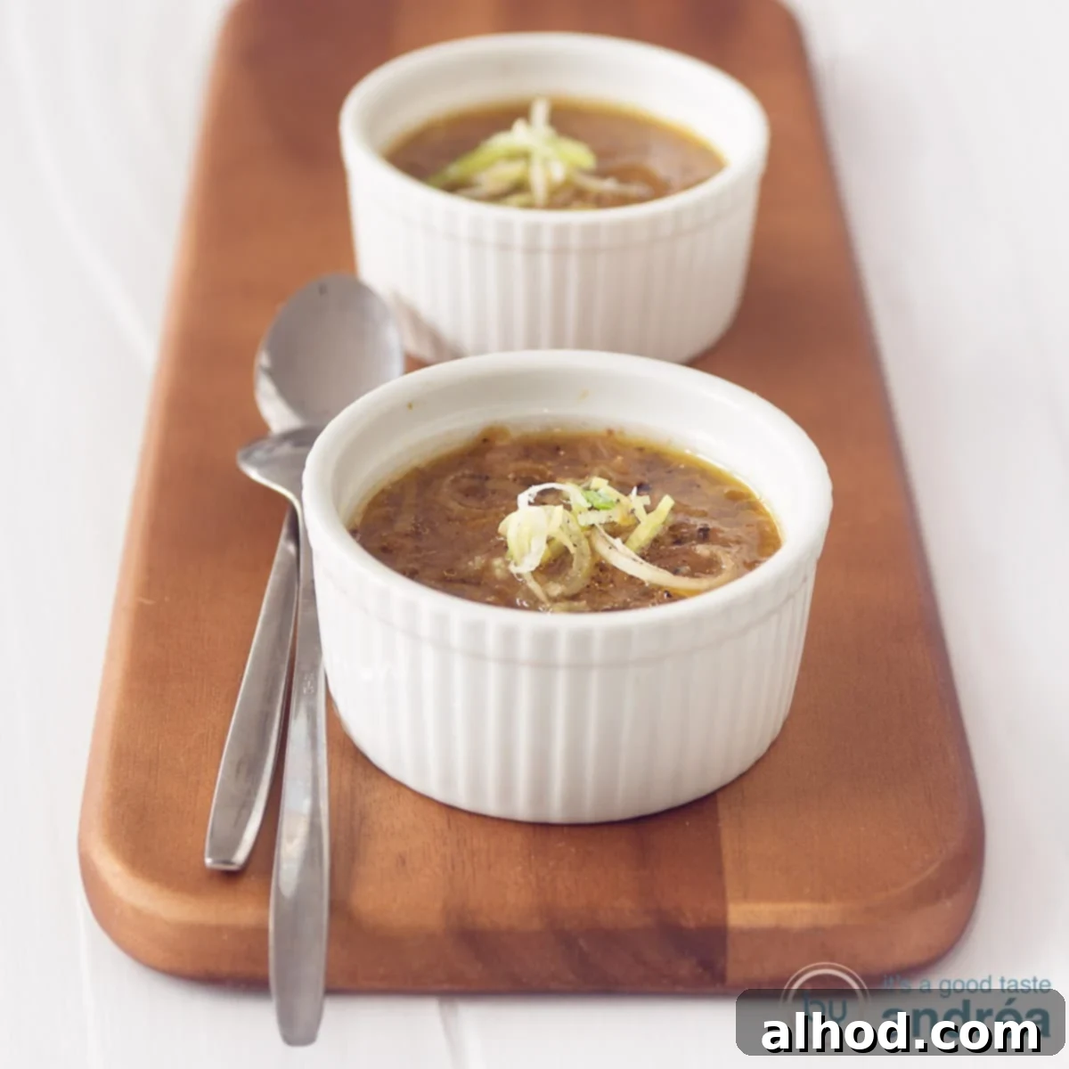 Hearty Vegetarian Cabbage Leek Soup 5 A square photo with two bowls filled with leek soup with cabbage. Two spoons next to it on a wooden board. A white background.