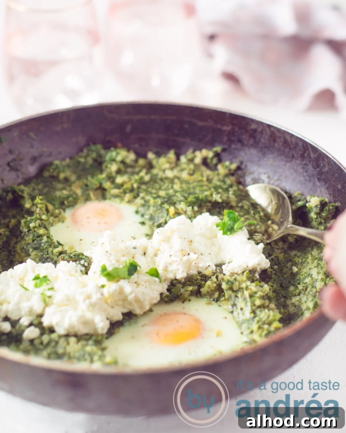 Silky Cauliflower Risotto with Fresh Spinach and Leeks 5 A black wok filled with a rich, creamy spinach, leek, and cauliflower rice dish, generously topped with two perfectly poached eggs and a dollop of fresh cottage cheese, served on a white background with a spoon taking a delectable bite.