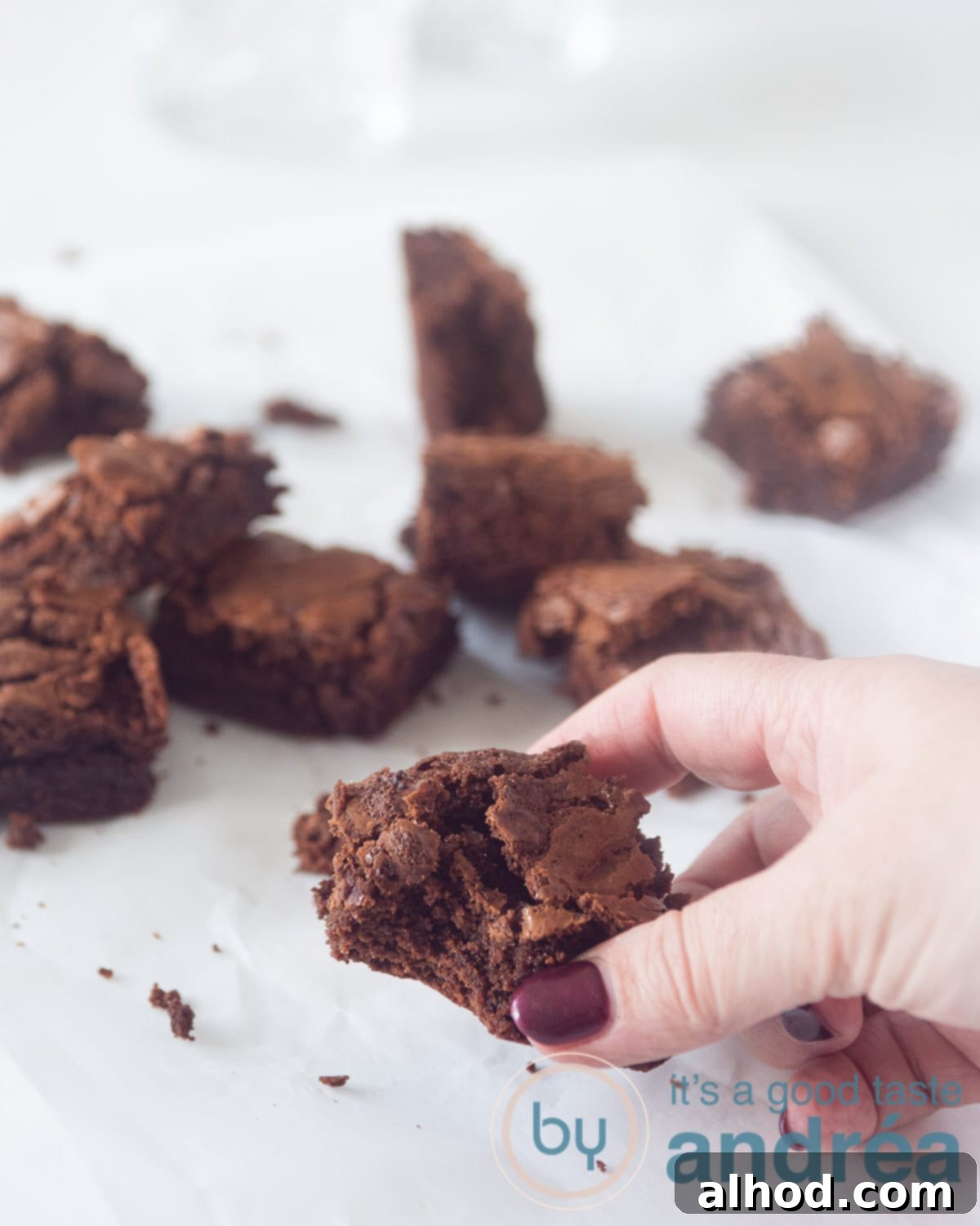Master Fudgy Brownies in 4 Simple Steps 2 A hand taking a brownie from a white surface. Some cubes of brownies scattering around