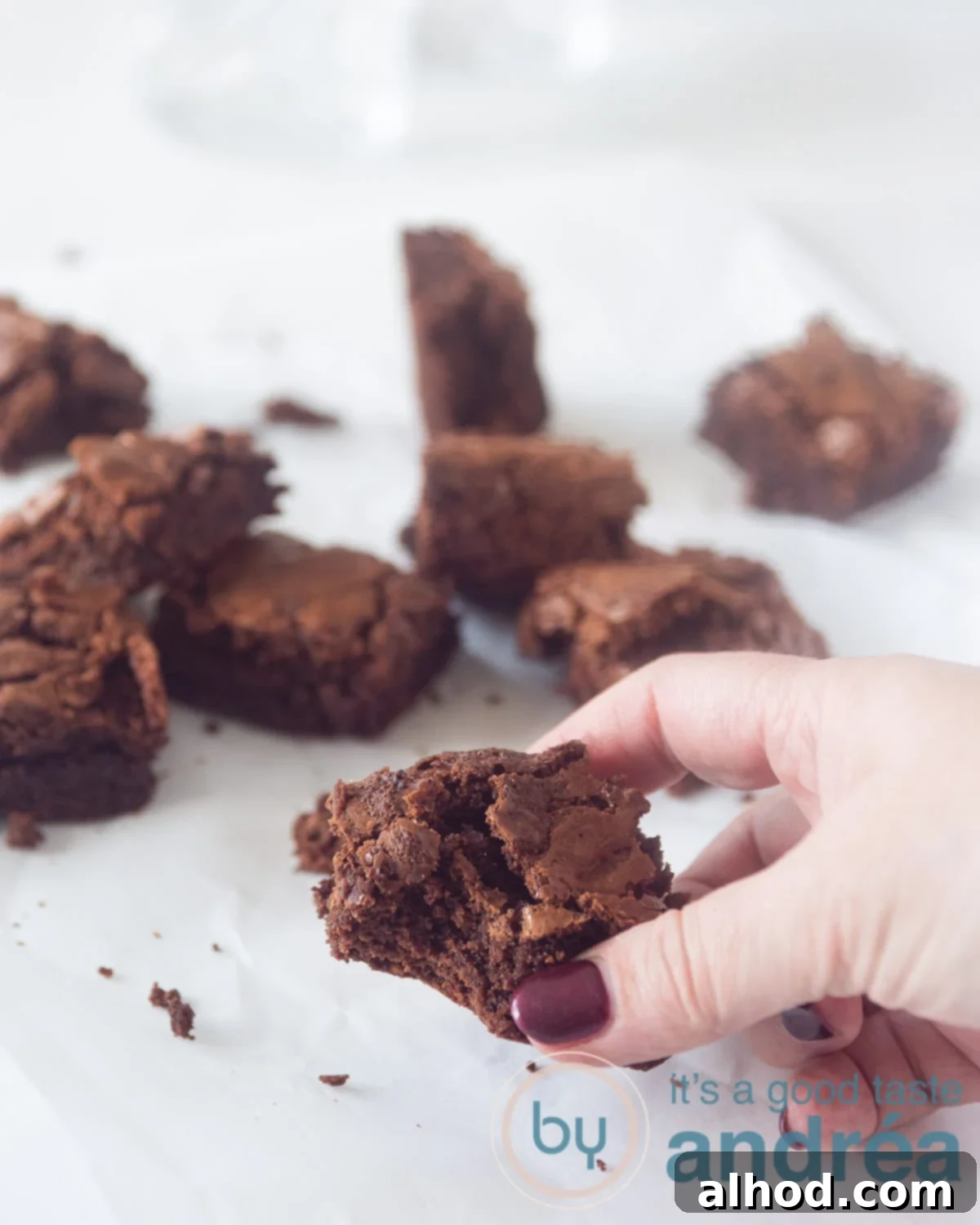 Master Fudgy Brownies in 4 Simple Steps 2 A hand taking a brownie from a white sufrace. Some cubes of brownies scattering around