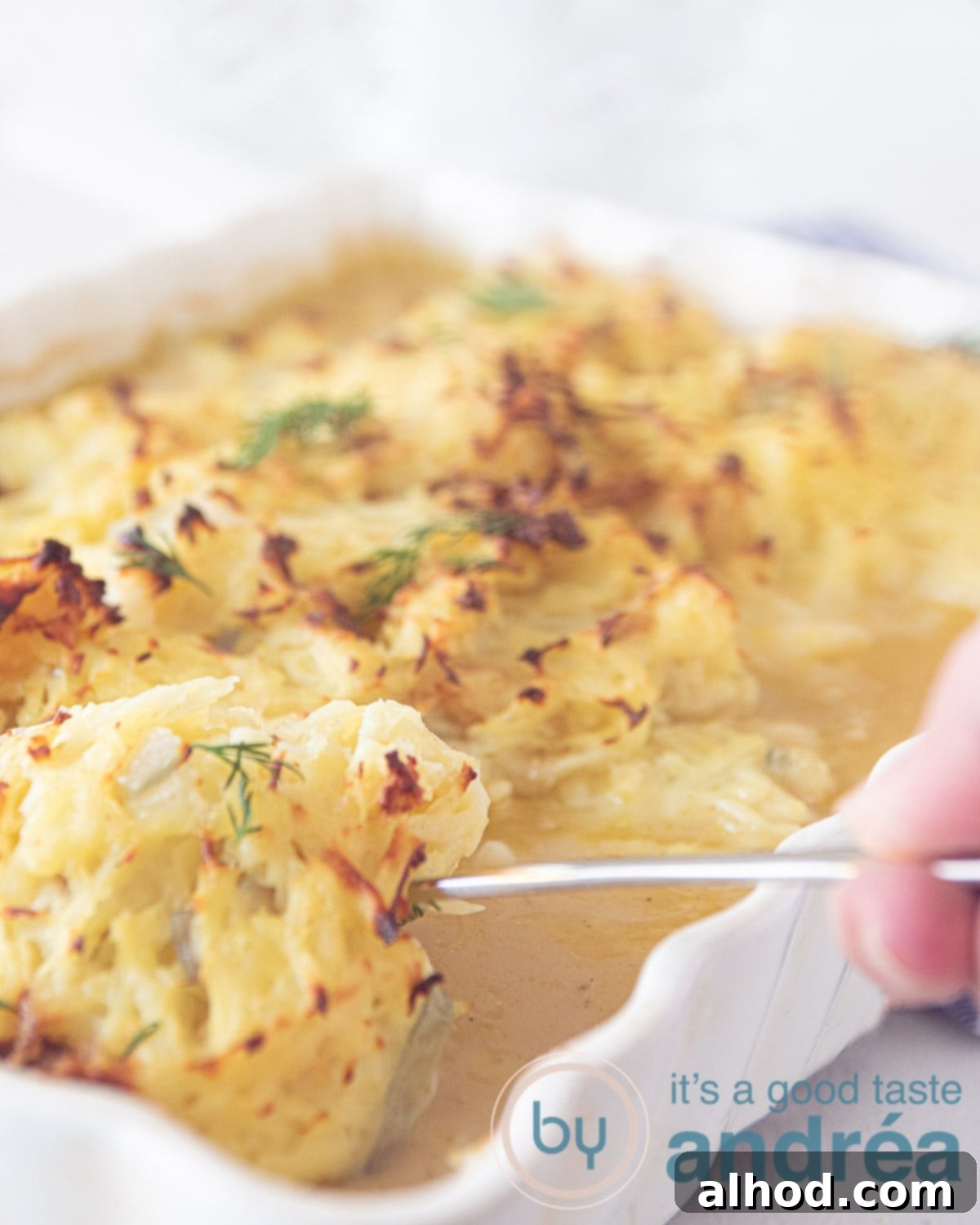 Hearty Cod and Potato Bake 2 A hand taking out a perfectly baked cod filet with golden Rösti topping from a casserole dish, stewed in a creamy white wine sauce.