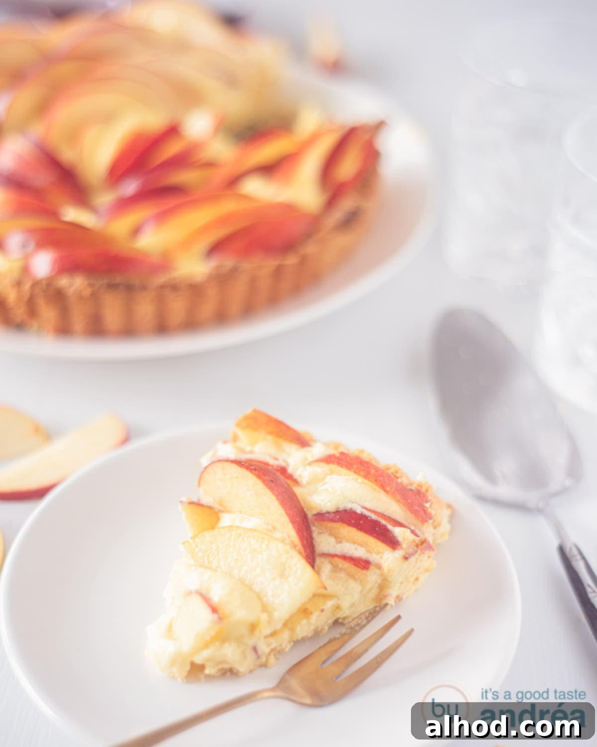 Rose Apple Delight 2 A slice of elegant Apple Rose Tart on a white plate with fresh apples and pastry cream in the background.