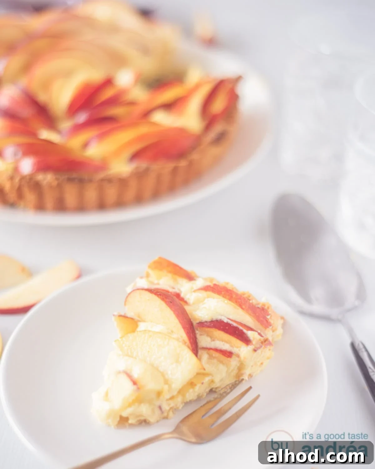 Rose Apple Tart 2 A slice of cake on a white plate with apples and pastry cream. In the background the rest of the cake on a plate.