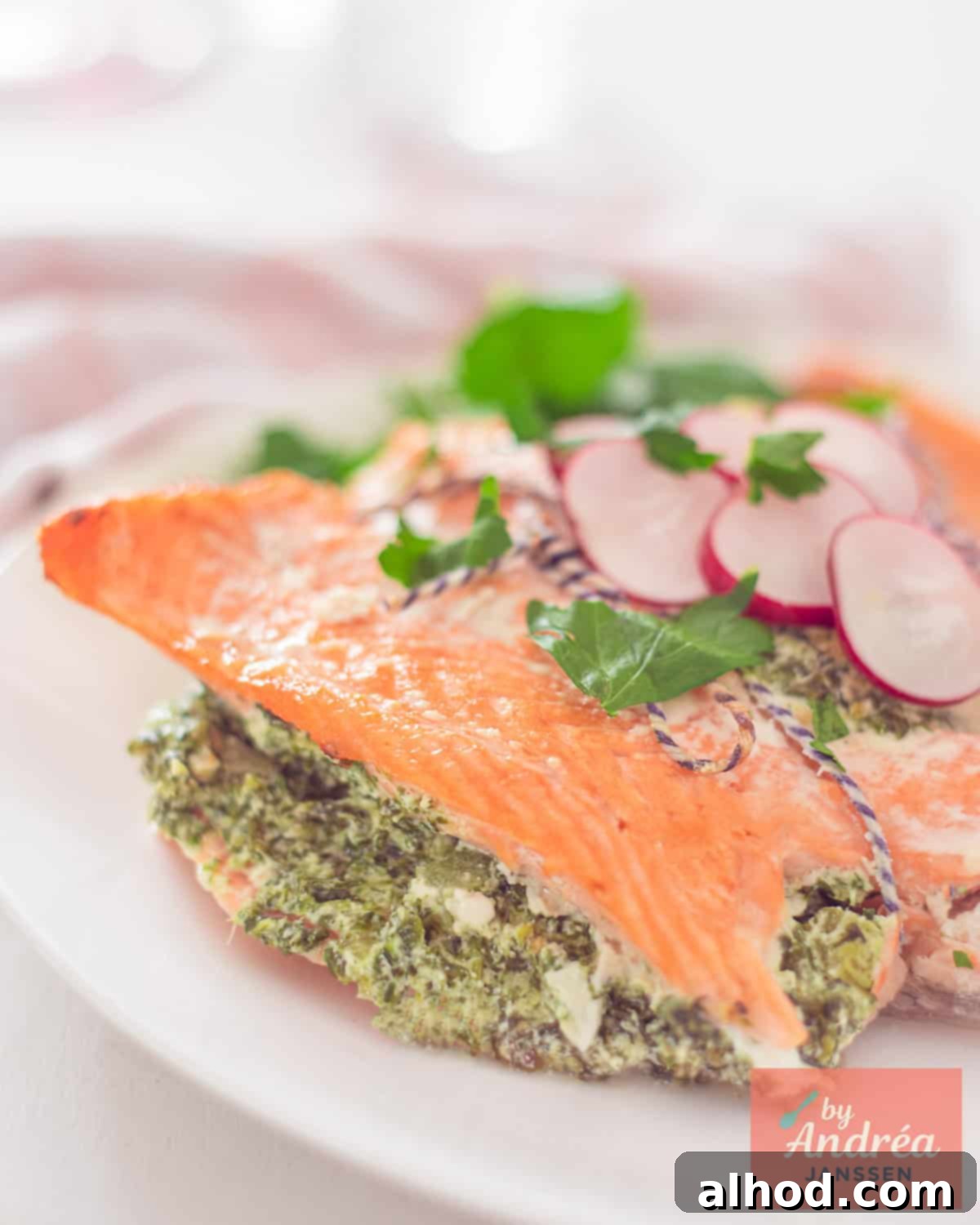 A portion of a stuffed salmon fillet with spinach and celery on a white plate, garnished with fresh herbs.