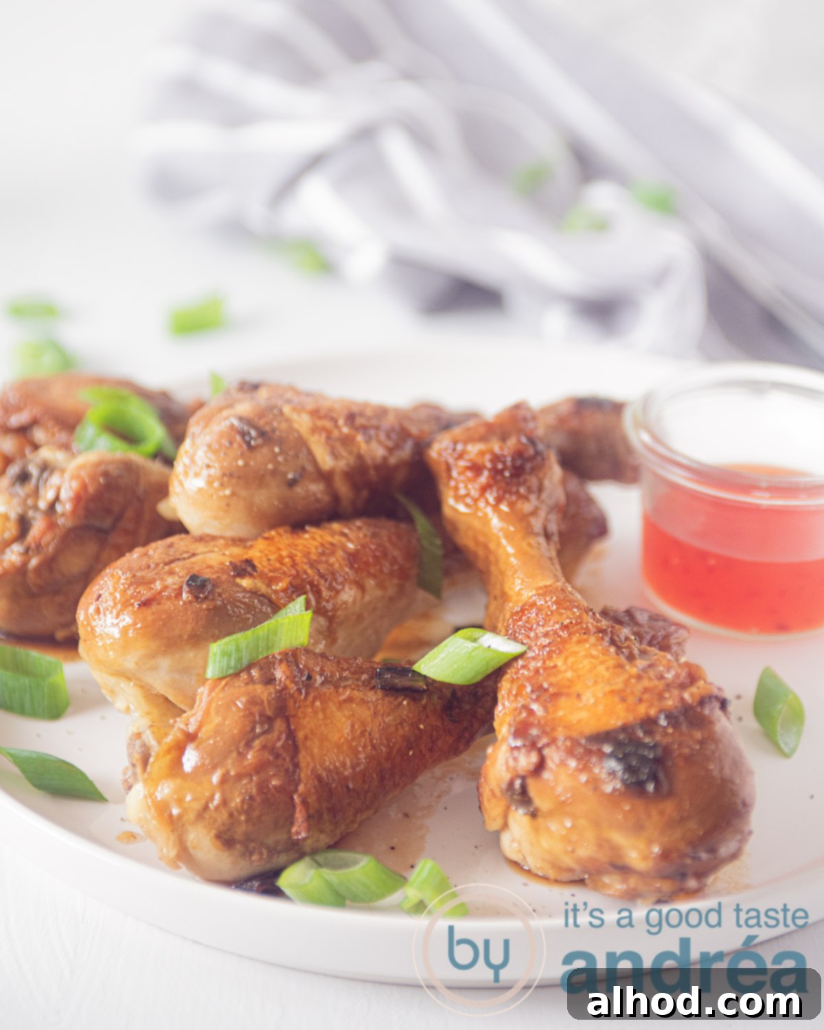 Sticky Soy Glazed Drumsticks 5 A white plate showcasing beautifully glazed soy sauce chicken drumsticks, with a small glass bowl of sweet chili sauce on the side for dipping. The dish is inviting and colorful.