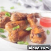 Sticky Soy Glazed Drumsticks 6 A square photo of a white plate with five chicken drumsticks in soy sauce, garnished with fresh spring onion and served alongside a small bowl of sweet chili sauce.