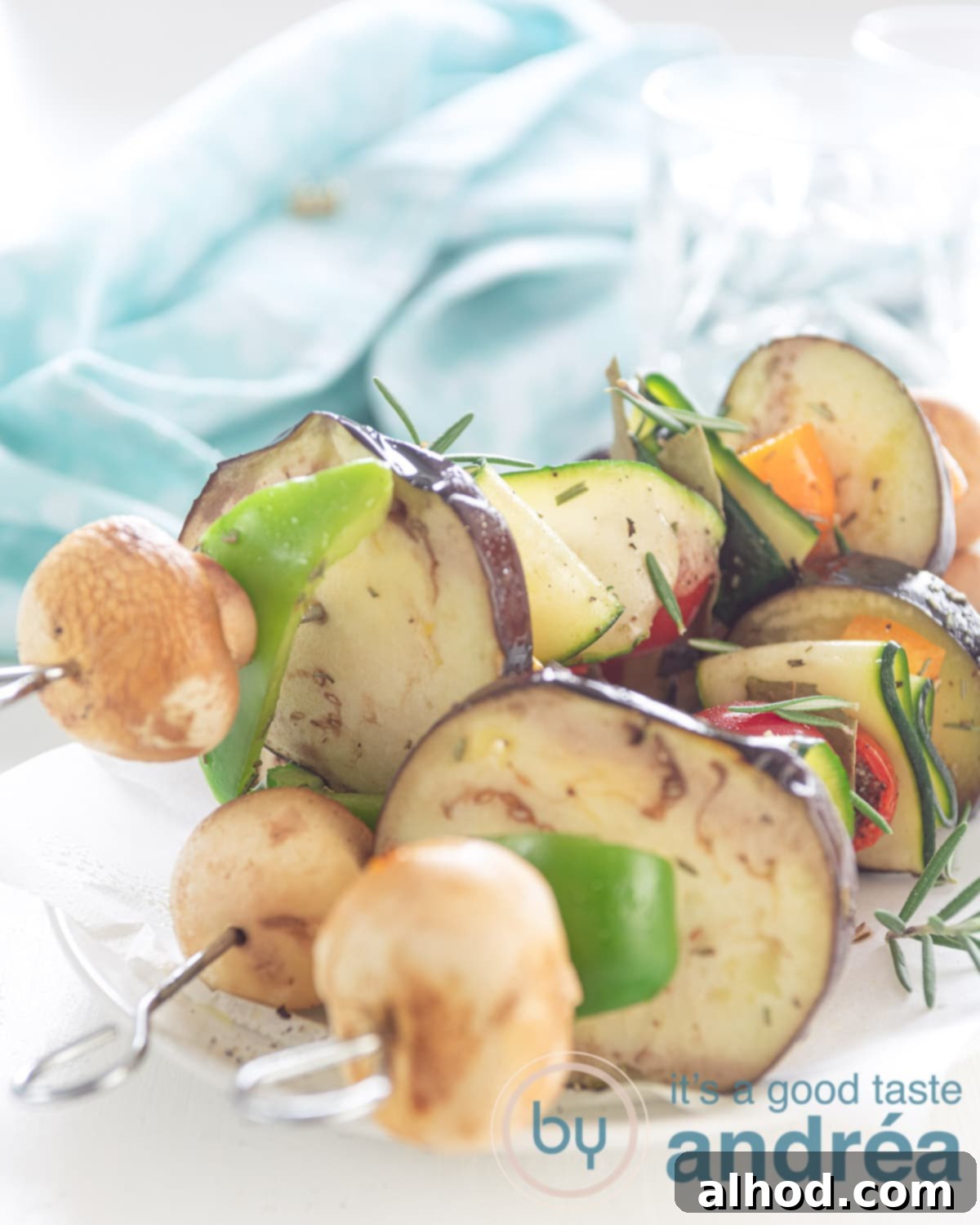 Three skewers with veggies that are grilled. A blue towel in the back