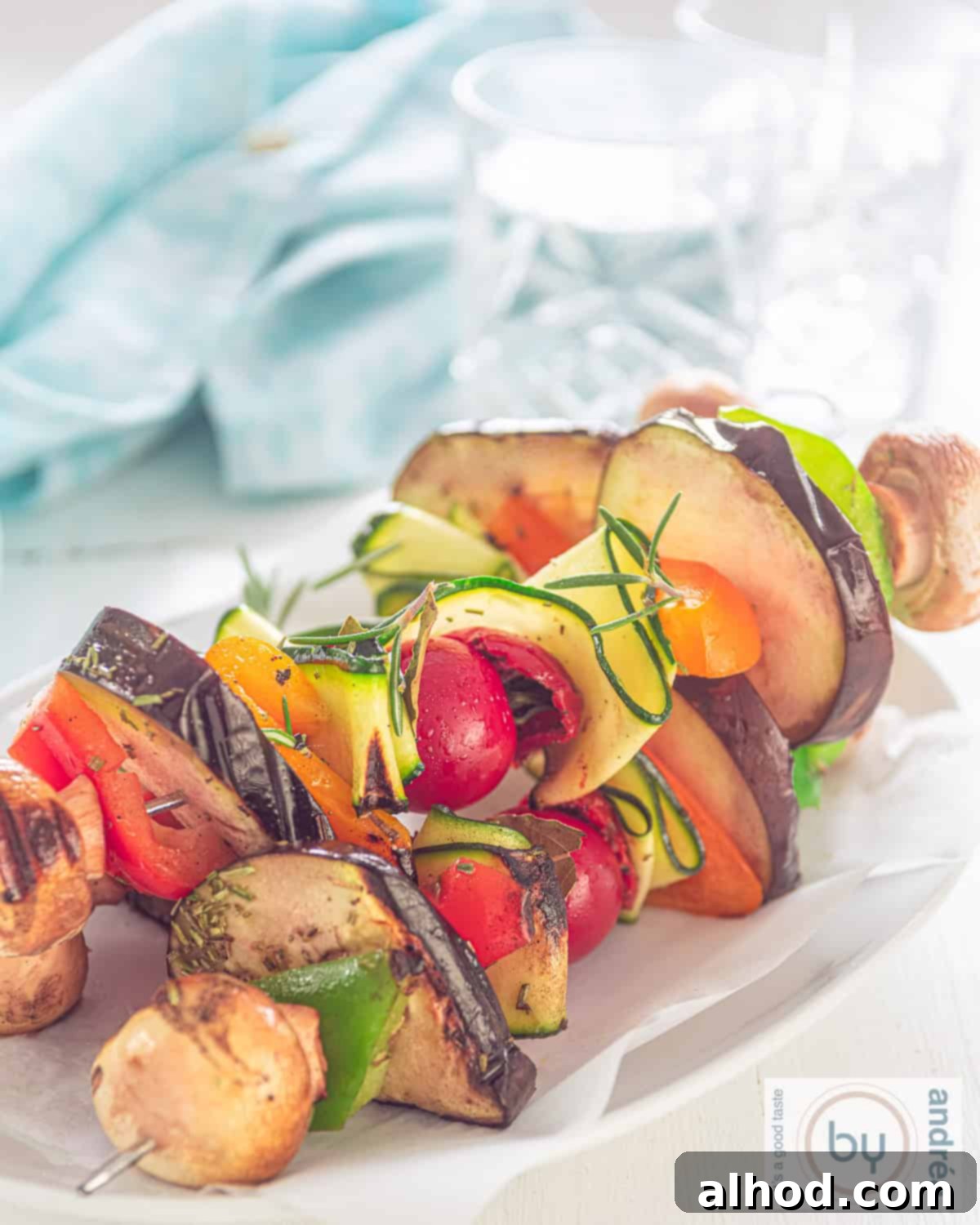 three vegan vegetable kebabs grilled, on a white plate. A Blue towel in the back