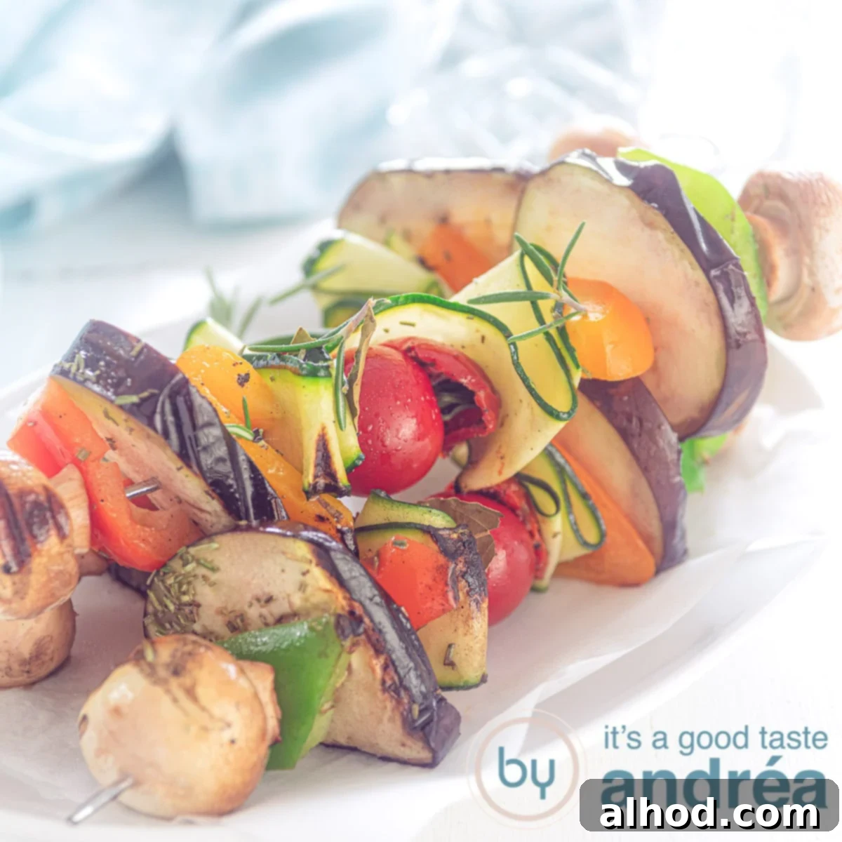Grilled Mediterranean Veggie Skewers 5 square photo with vegan vegetable kebobs on a white plate, three. A blue towel in the back.