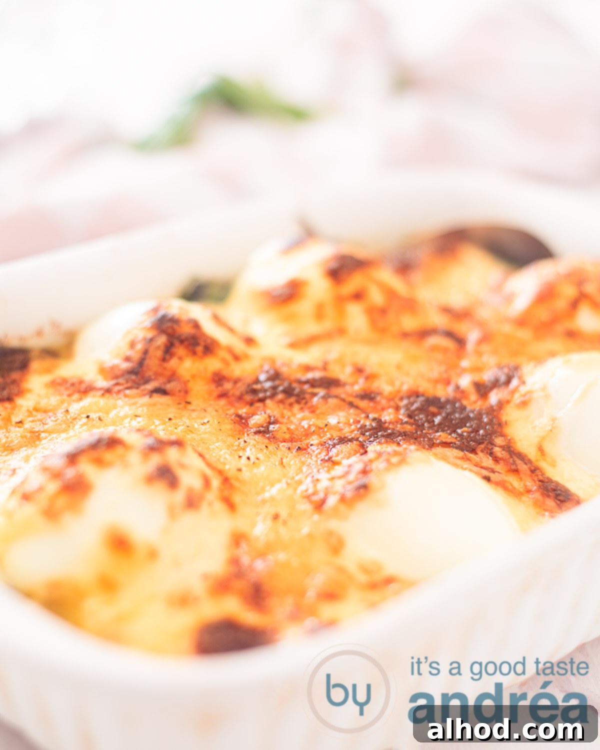 Classic Eggs Florentine 3 A white casserole filled with spinach, eggs, Mornay sauce and Gruyere gratin. A pink-white cloth in the back.