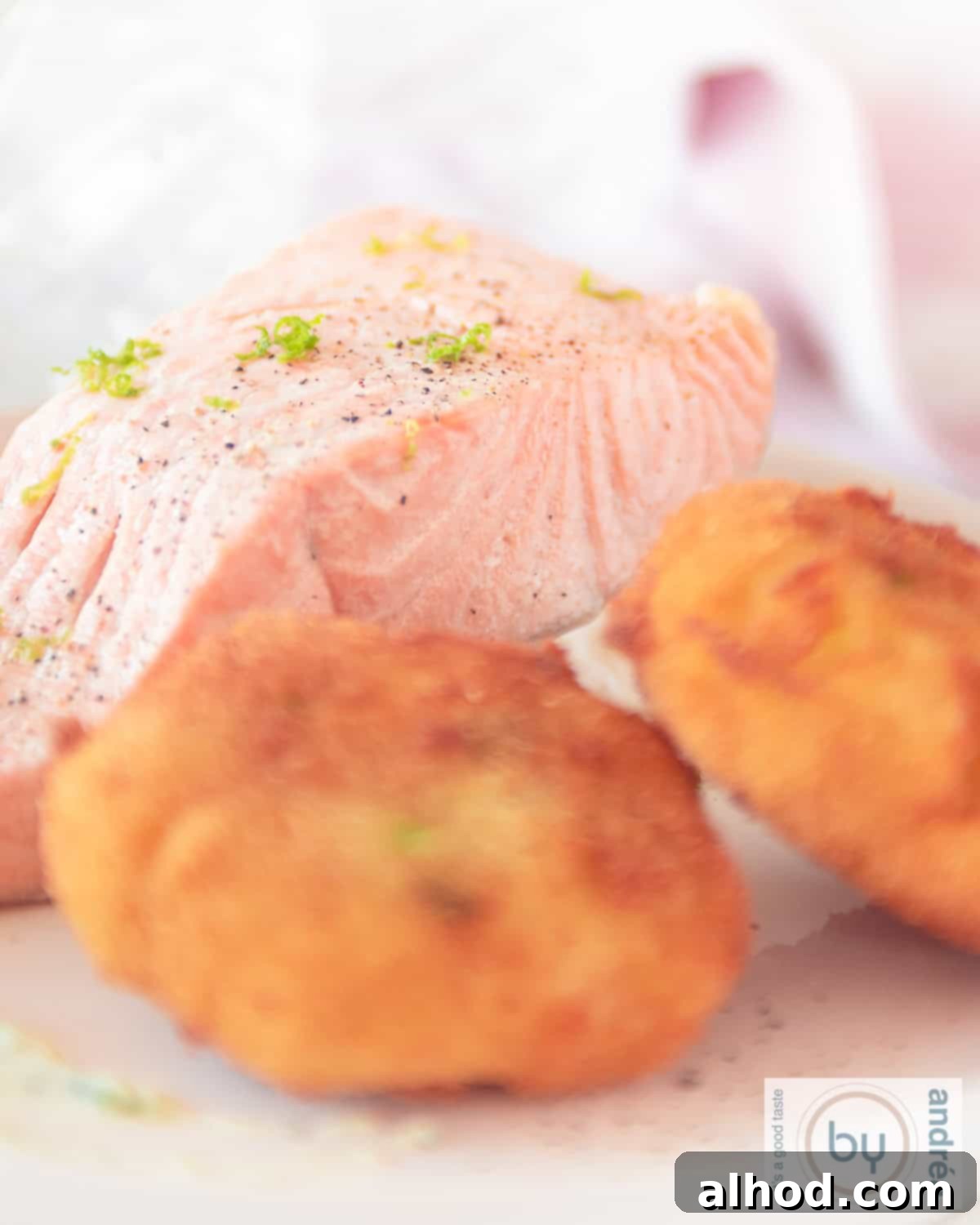 Wasabi-Spiked Smoked Salmon Latkes 2 A height photo with a portion of tea-smoked salmon and two golden-brown wasabi potato latkes, garnished with fresh herbs.