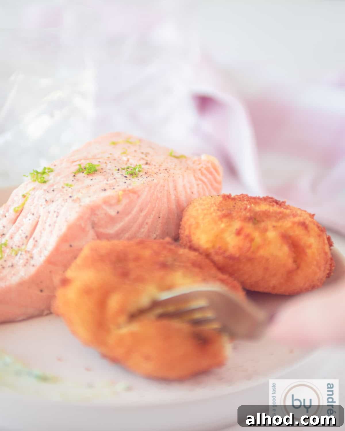 Wasabi-Spiked Smoked Salmon Latkes 5 A height photo of warm tea-smoked salmon and two golden-brown wasabi potato croquettes on a white plate. A fork is gently piercing one of the croquettes.