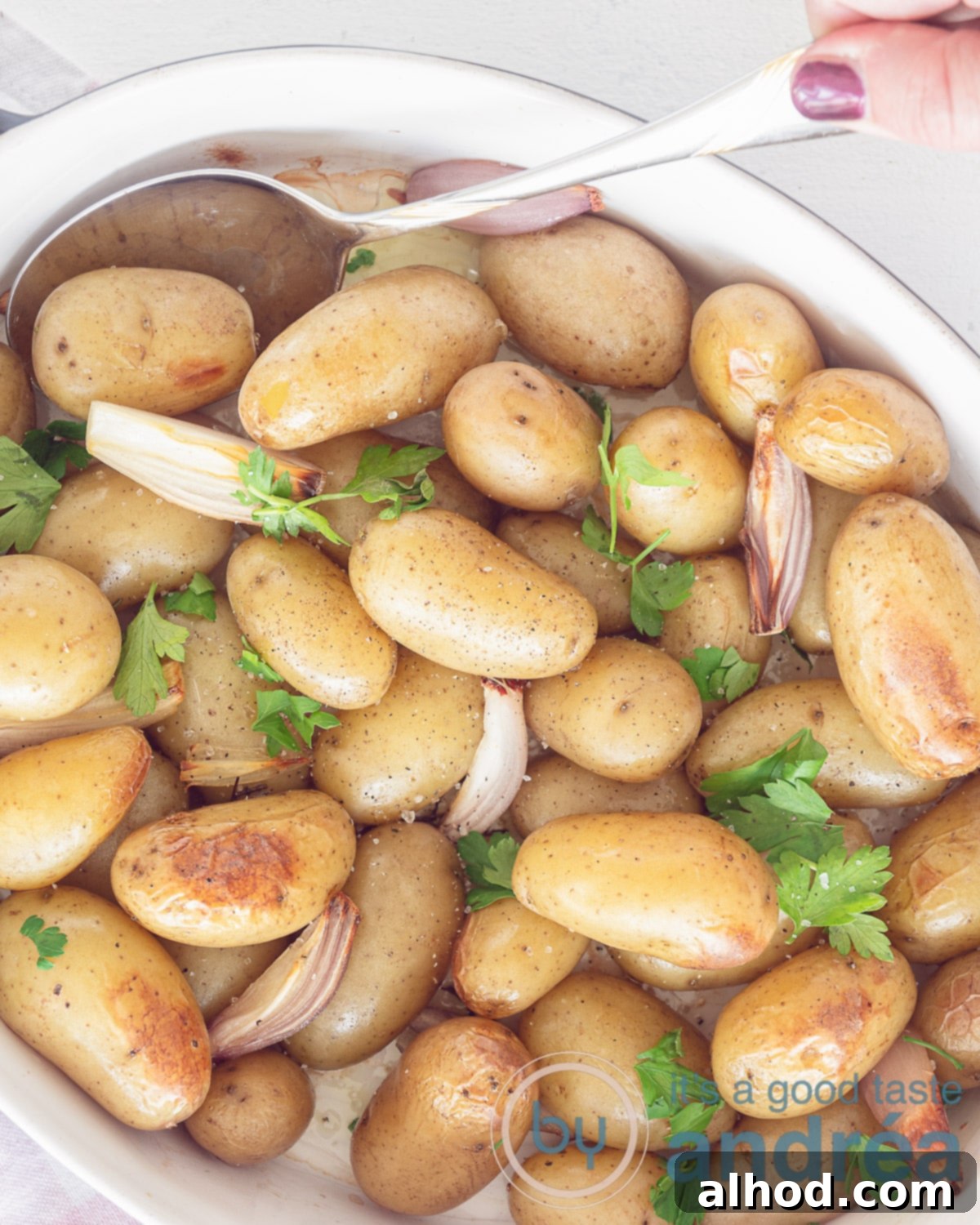 Golden Crispy Oven Roasted Baby Dutch Potatoes 2 A photo from above showing a white baking dish on a white background with oven-baked baby potatoes, parsley, garlic, and shallots, ready to serve.