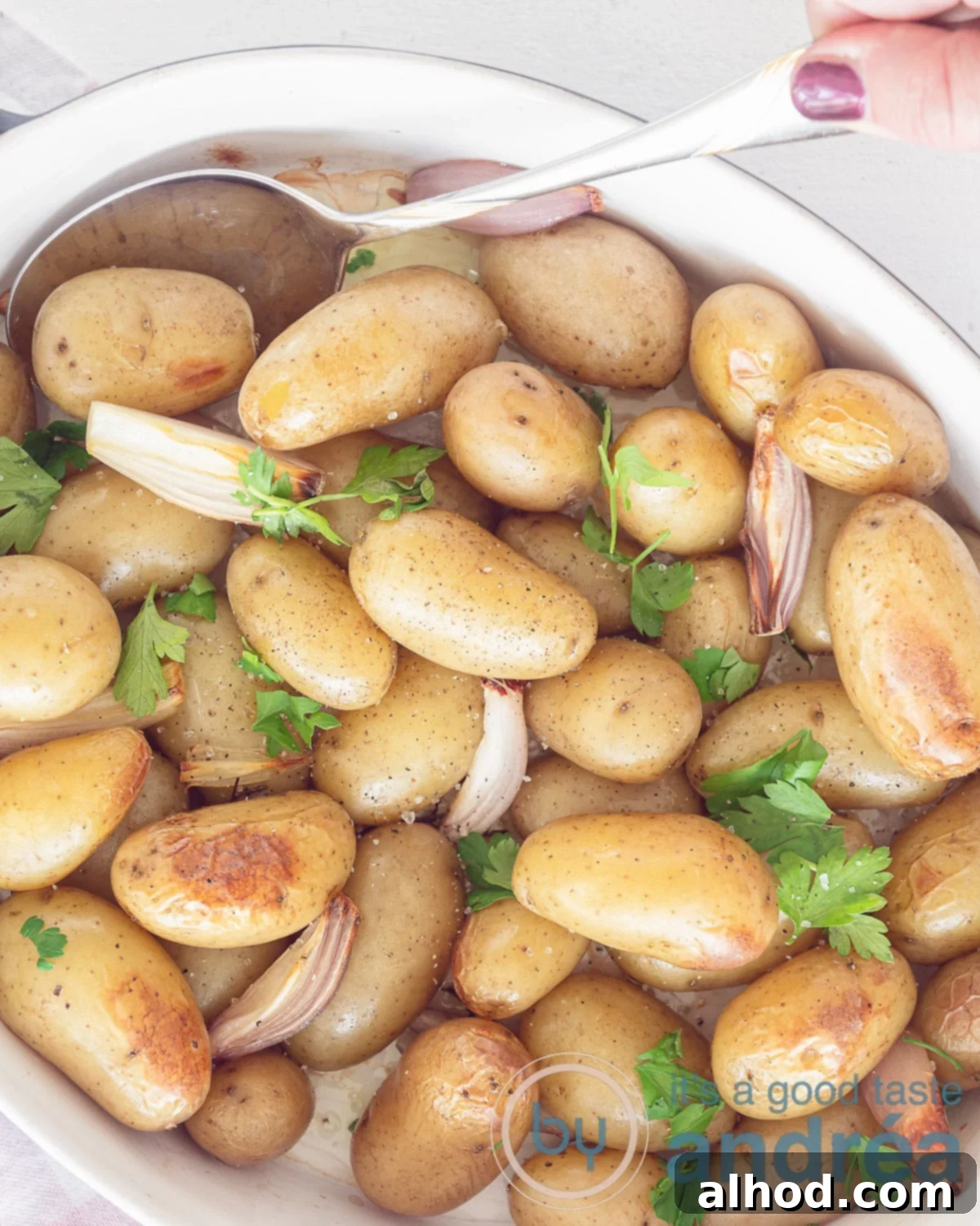 A photo from above showing a white baking dish on a white background with oven baked baby potatoes, parsley, garlic and shallots