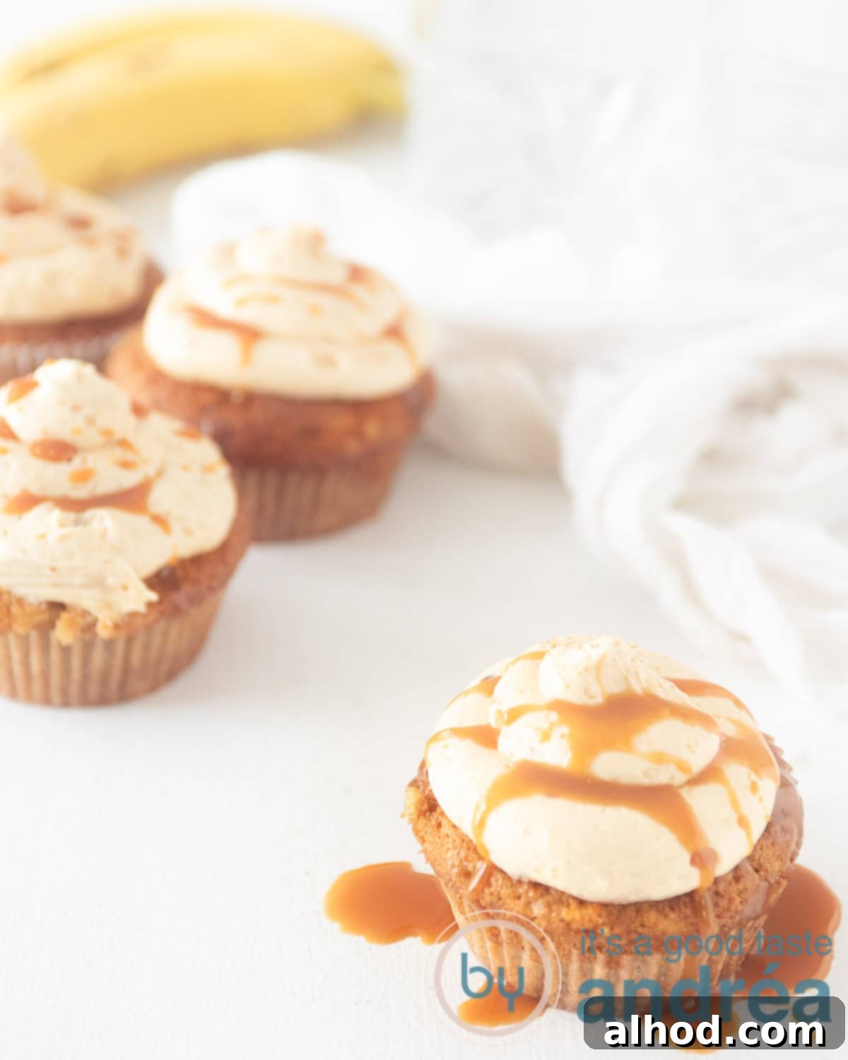 Deliciously moist banana cupcakes with a generous swirl of caramel buttercream and a drizzle of extra caramel sauce, ready to be enjoyed.