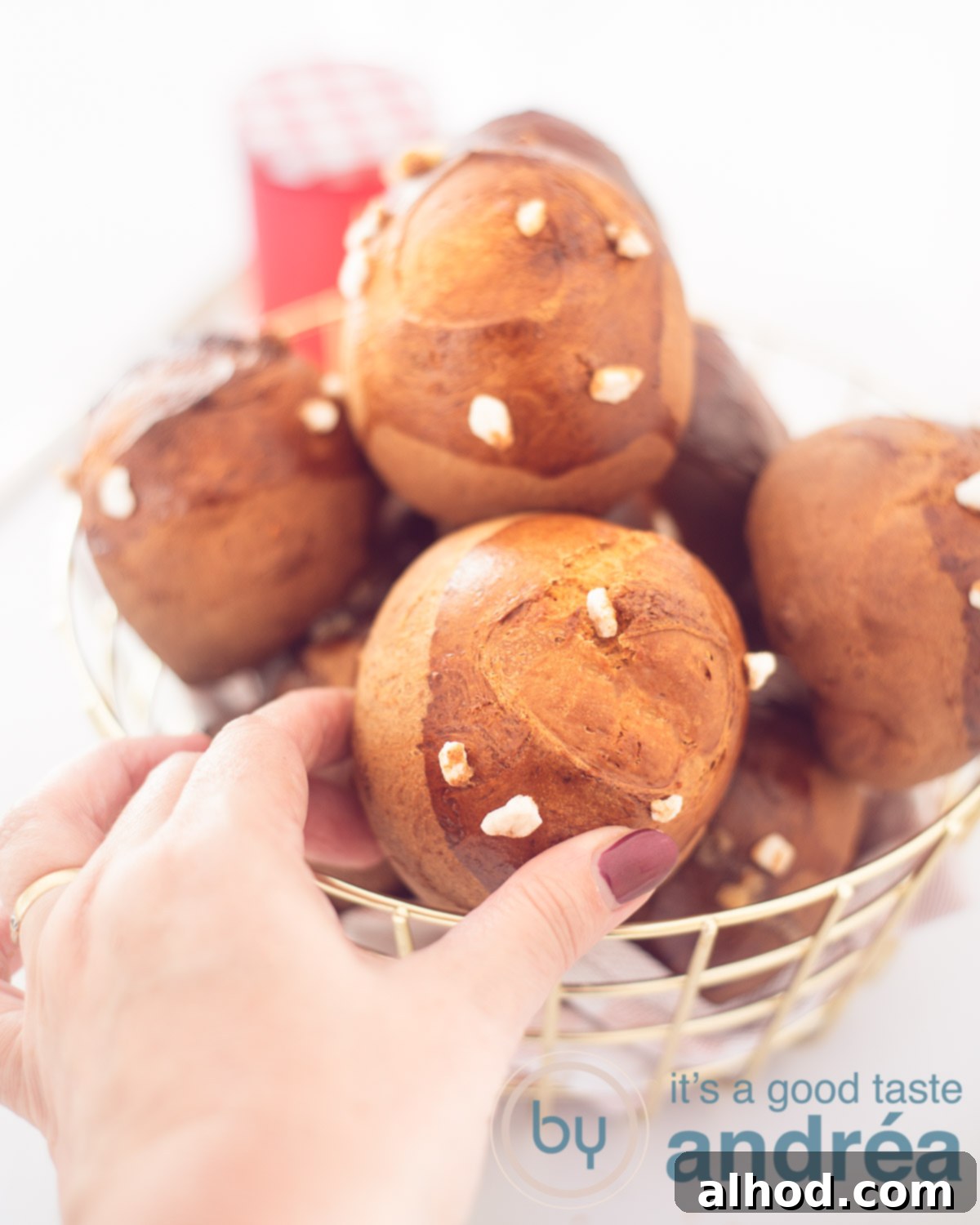 Dutch Pearl Sugar Buns 5 A golden wire basket filled with sugar buns on a white background. A hand grabs a bun.