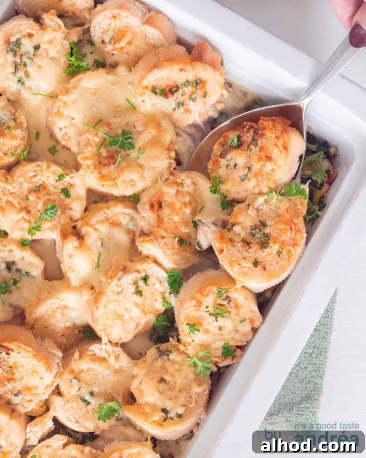 Creamy Chicken and Leek Comfort Bake 2 A white baking dish filled with chicken leek and covered with slices of baguette with gratinated cheese. A spoon sticks in it.