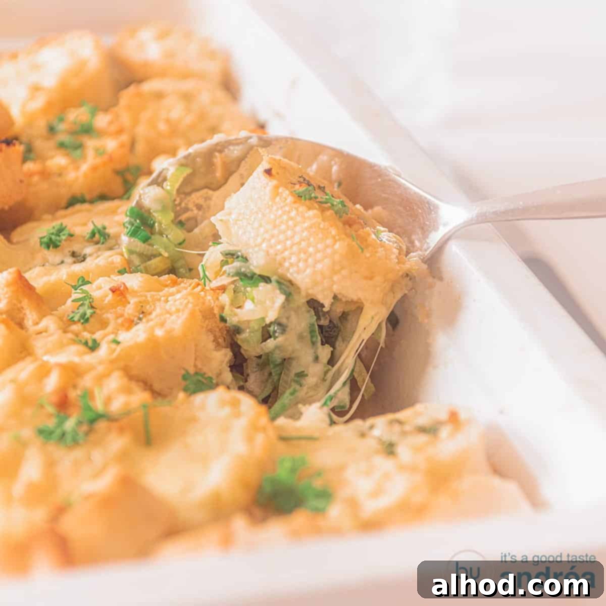 Creamy Chicken and Leek Comfort Bake 5 A square photo with a white baking dish. A scoop of chicken leek and a baguette are scooped out. Cheese gratin.