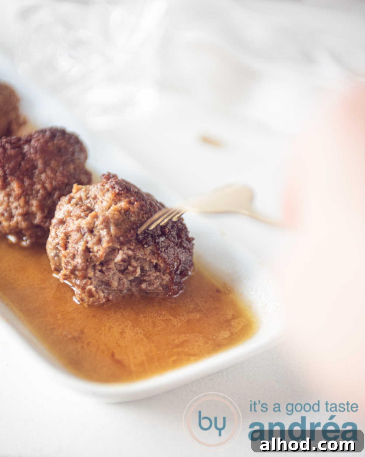 Granny's Authentic Dutch Meatballs 4 Three perfectly browned and braised Dutch meatballs resting in a row on a white plate, glistening with rich gravy.