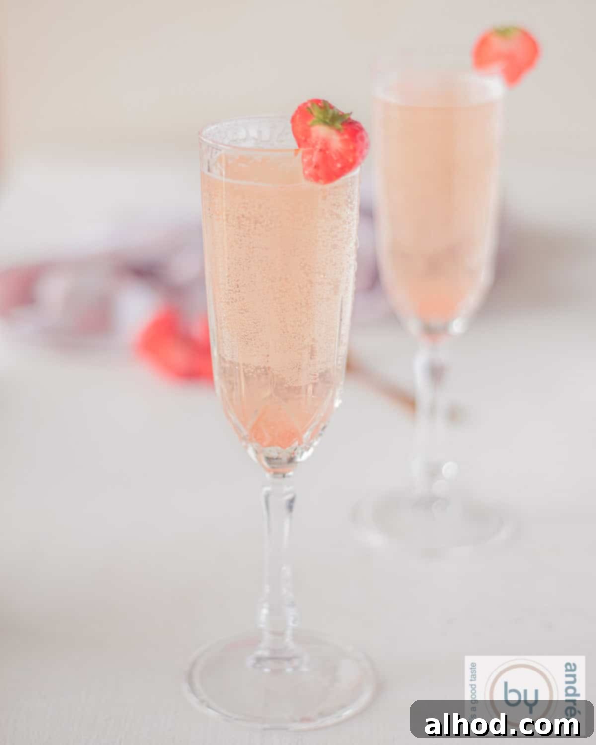 Bubbly Strawberry Bellini Delight 2 Two glasses filled with Valentine's cocktail: strawberries and prosecco on a white background. In the background a pink and white tea towel and strawberries