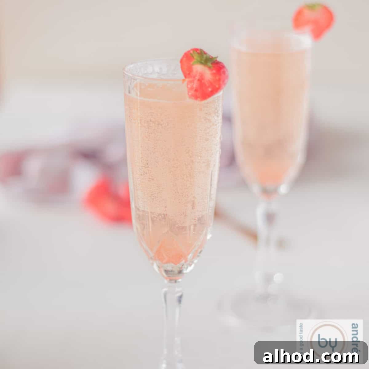 Bubbly Strawberry Bellini Delight 4 A square photo of two champagne flutes filled with strawberry prosecco cocktail with a strawberry garnish.