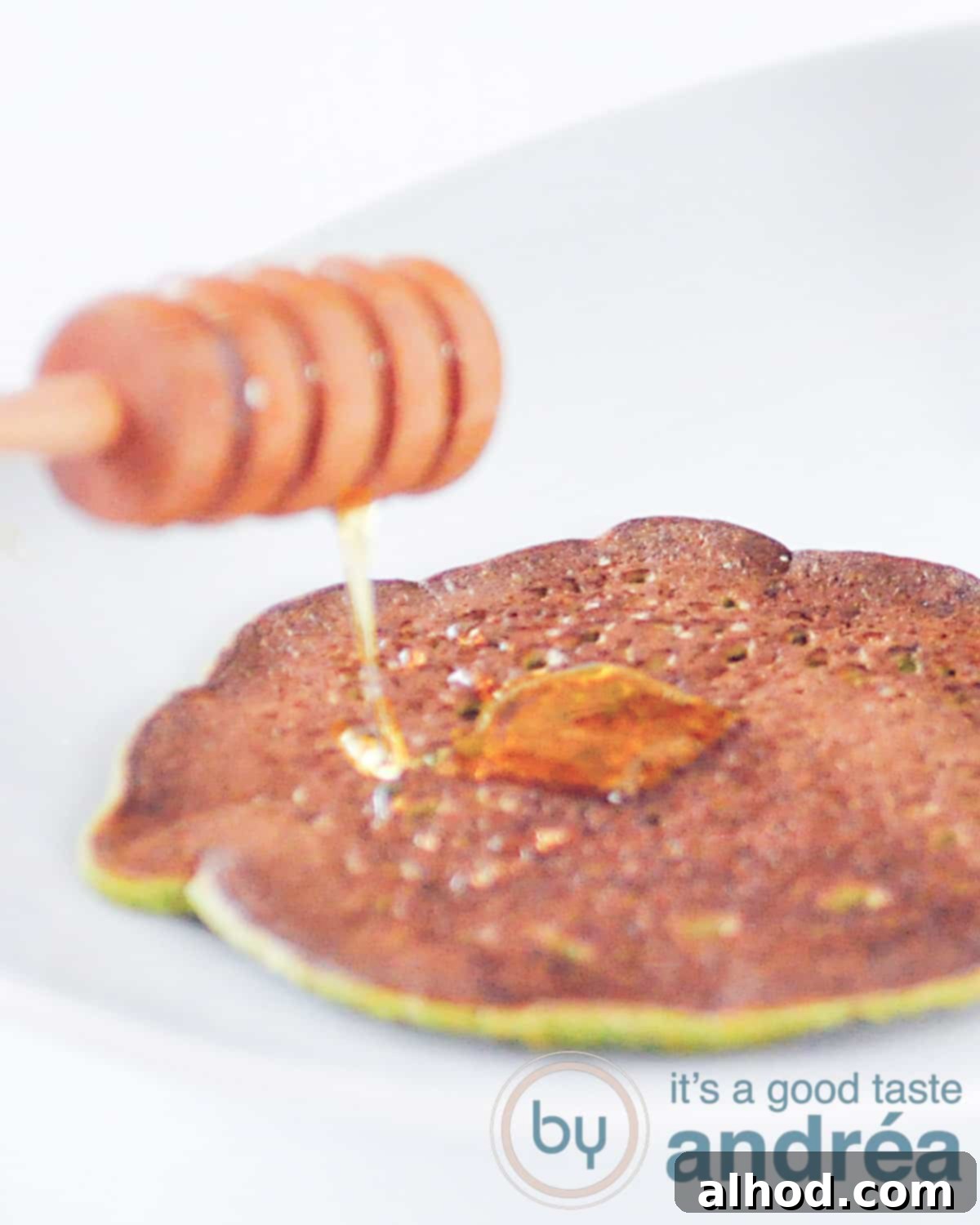 A stack of fluffy green spinach pancakes on a white plate, with golden honey drizzled over the top. The plate rests on a clean white background, highlighting the fresh, wholesome appearance of the breakfast.