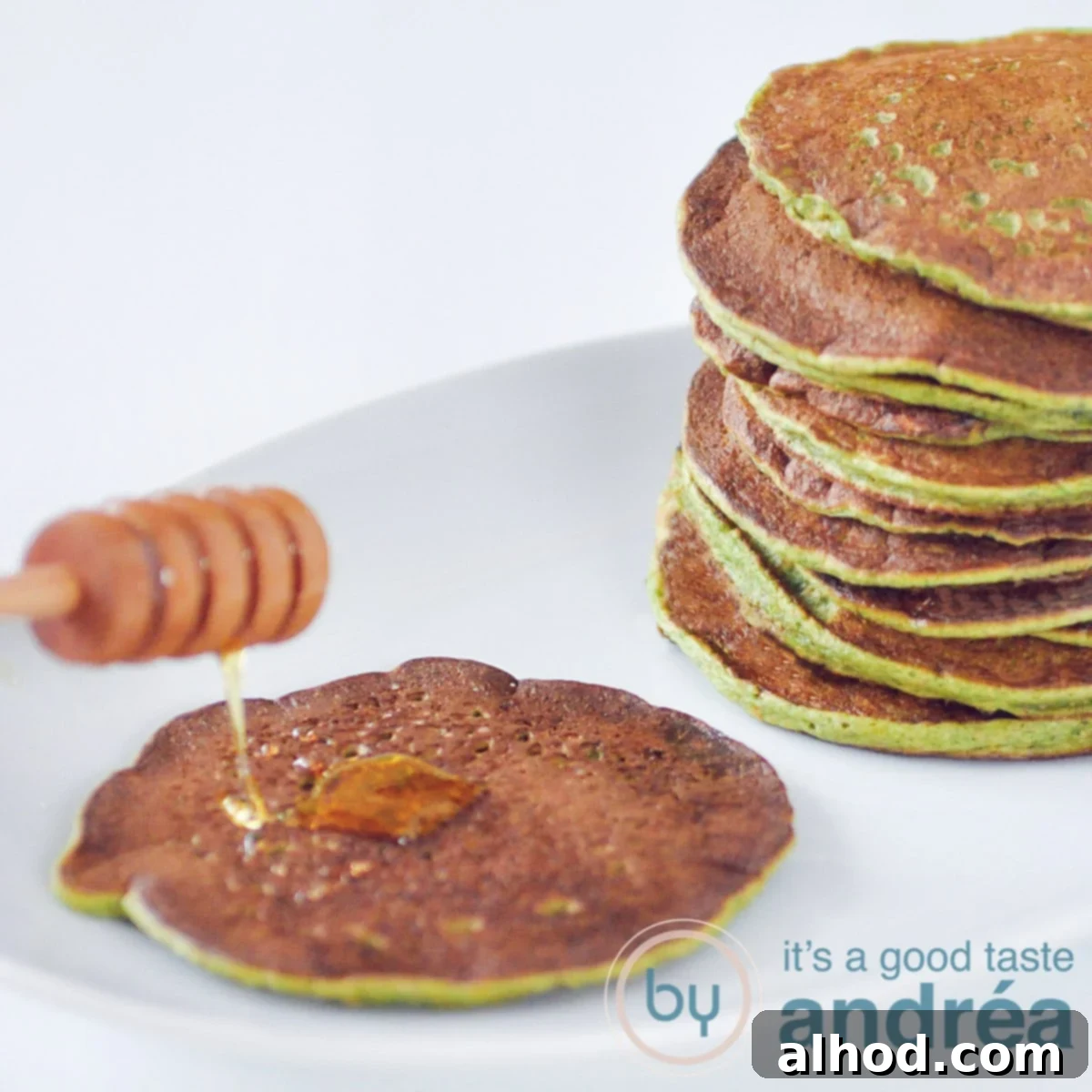 A square photo showing a stack of healthy whole wheat spinach pancakes, with one pancake topped with a generous drizzle of honey.