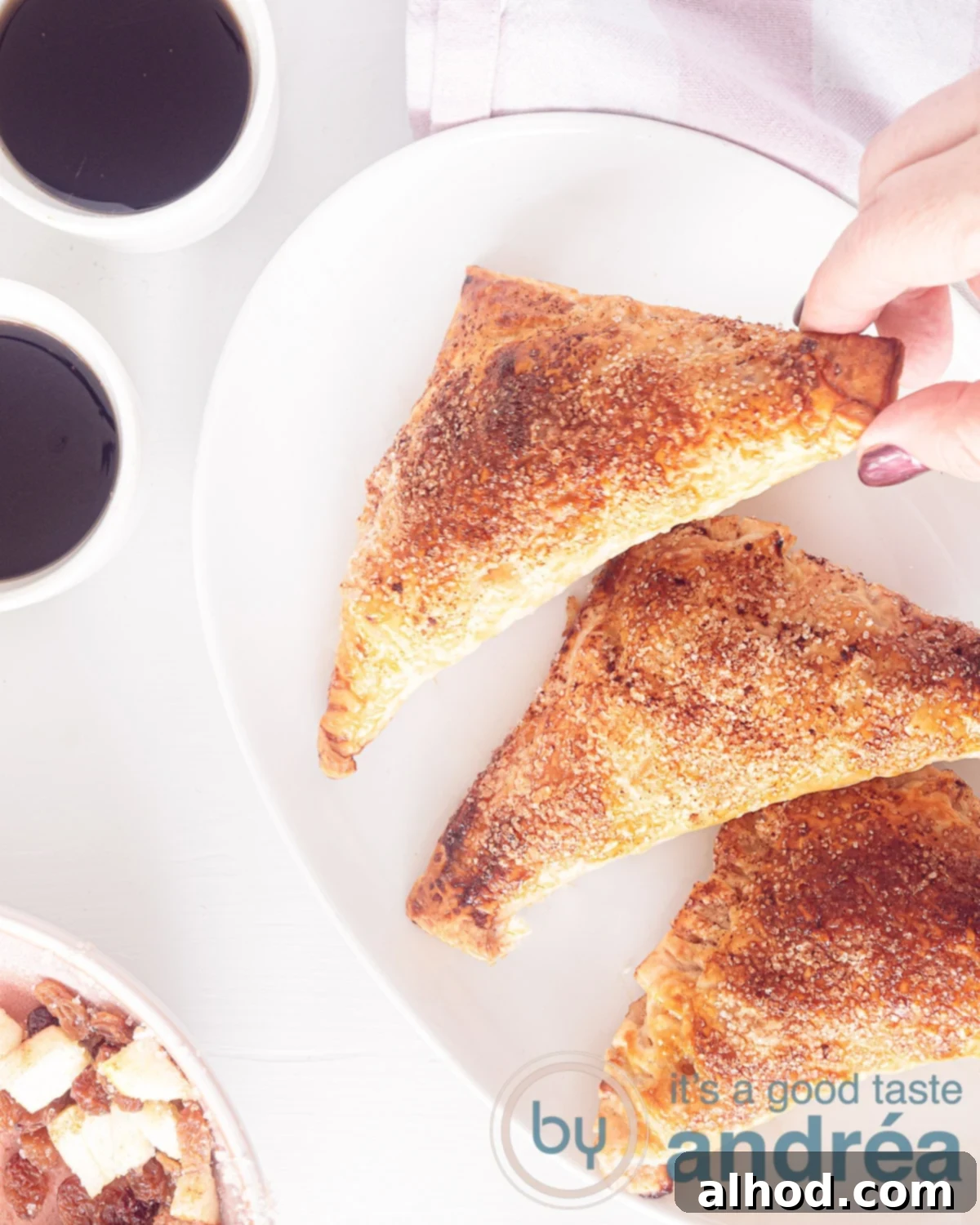 Appelflappen Dutch Apple Turnovers 2 A photo taken from above of a white bowl with three apple turnovers, two white mugs with coffee on a white background