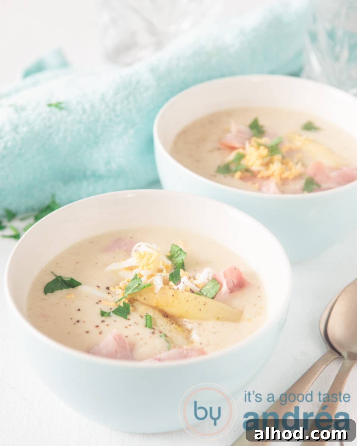Velvety Dutch White Asparagus Soup 2 Two white bowls filled with a creamy asparagus soup and topped with ham and grated egg, highlighting its luxurious texture and vibrant garnish.