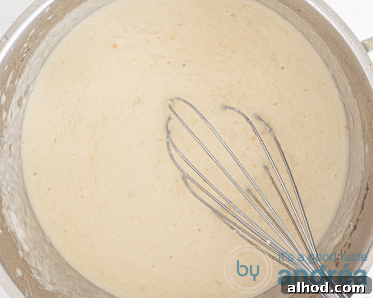 Velvety Dutch White Asparagus Soup 7 A close-up of a whisk stirring the creamy Dutch white asparagus soup in a pot, showing its smooth texture.