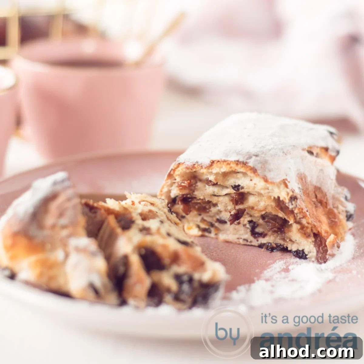 Zesty Orange Cinnamon Easter Stollen 3 A square photo with an Easter stolly opened, so you see the inside with raisins, currants and orange. Background a pink cup with coffee and a bread basket.