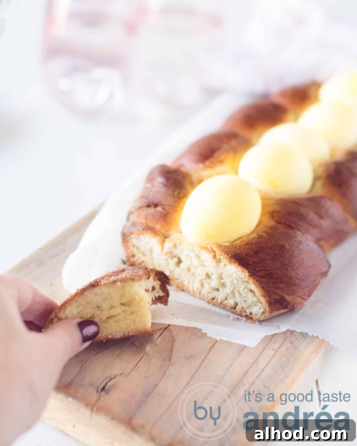 Greek Easter Tsoureki Bread 2 Tsoureki, topped with yellow eggs. A slice cut of. A hand taken the slice. A white background.