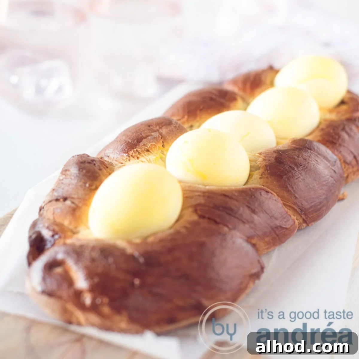 Greek Easter Tsoureki Bread 6 A square picture with Greek Easter bread topped with yellow eggs, on a white baking paper. A white background