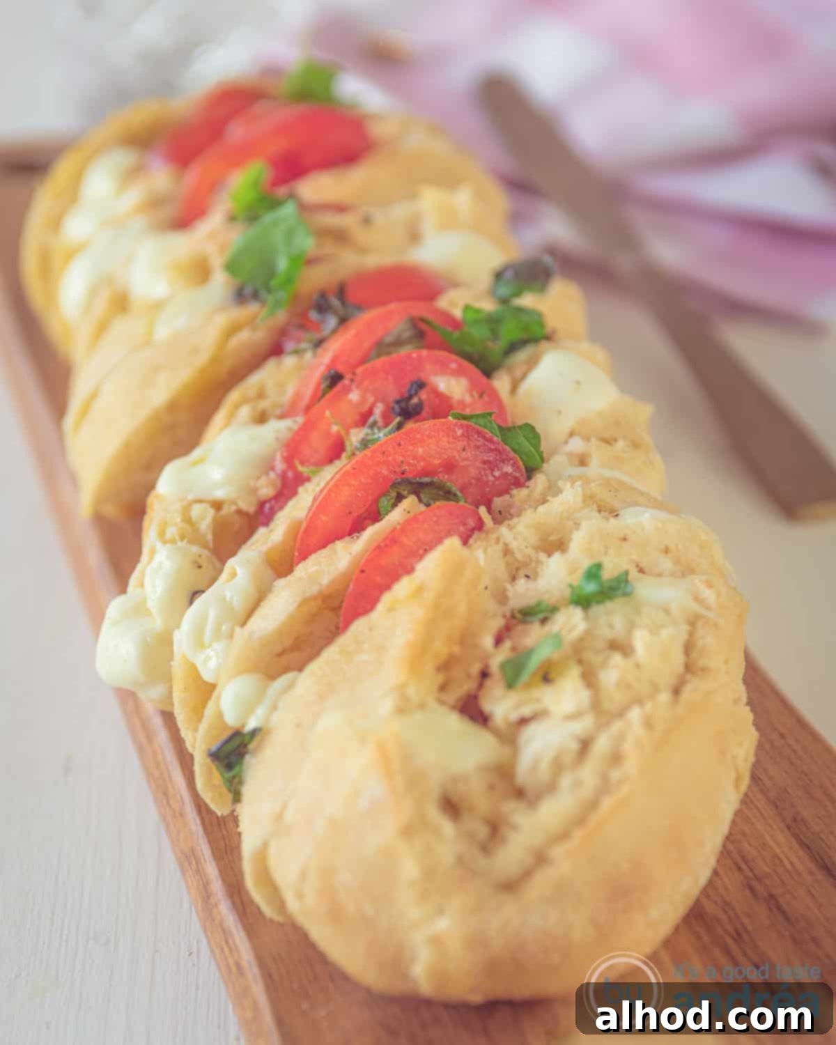 Fresh and Flavorful Caprese Baguette 2 A wooden board with a stuffed baguette with tomato, mozzarella and basil on a wooden board. A white background.