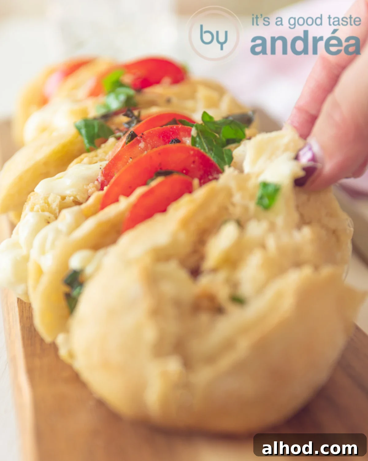 Fresh and Flavorful Caprese Baguette 3 A filled caprese baguette with mozzarella, tomatoes and basil, a hand taking a slice. On a wooden board.