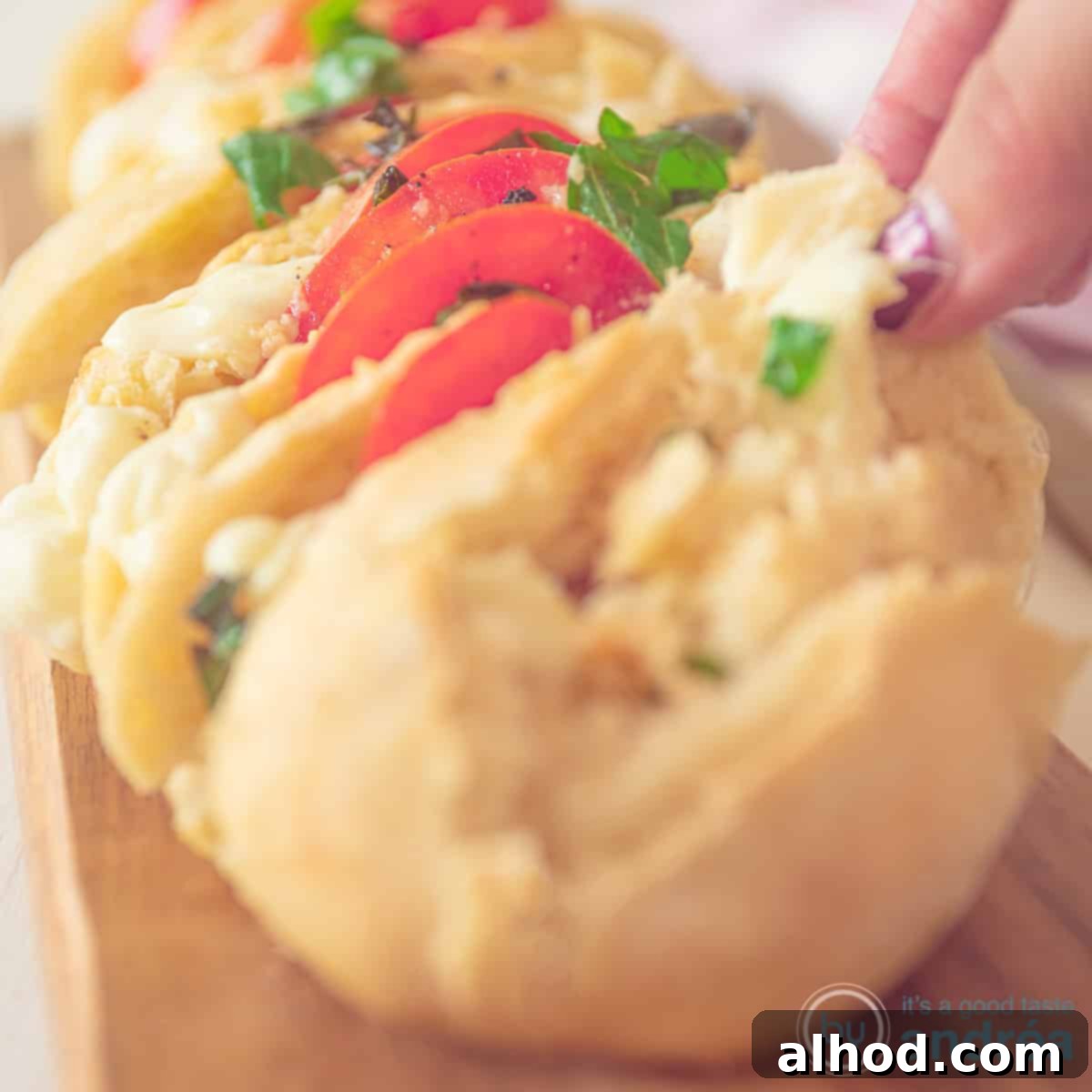 Fresh and Flavorful Caprese Baguette 4 A square photo with part of a stuffed baguette filled with tomato, mozzarella and basil. A hand grabs a slice of baguette.