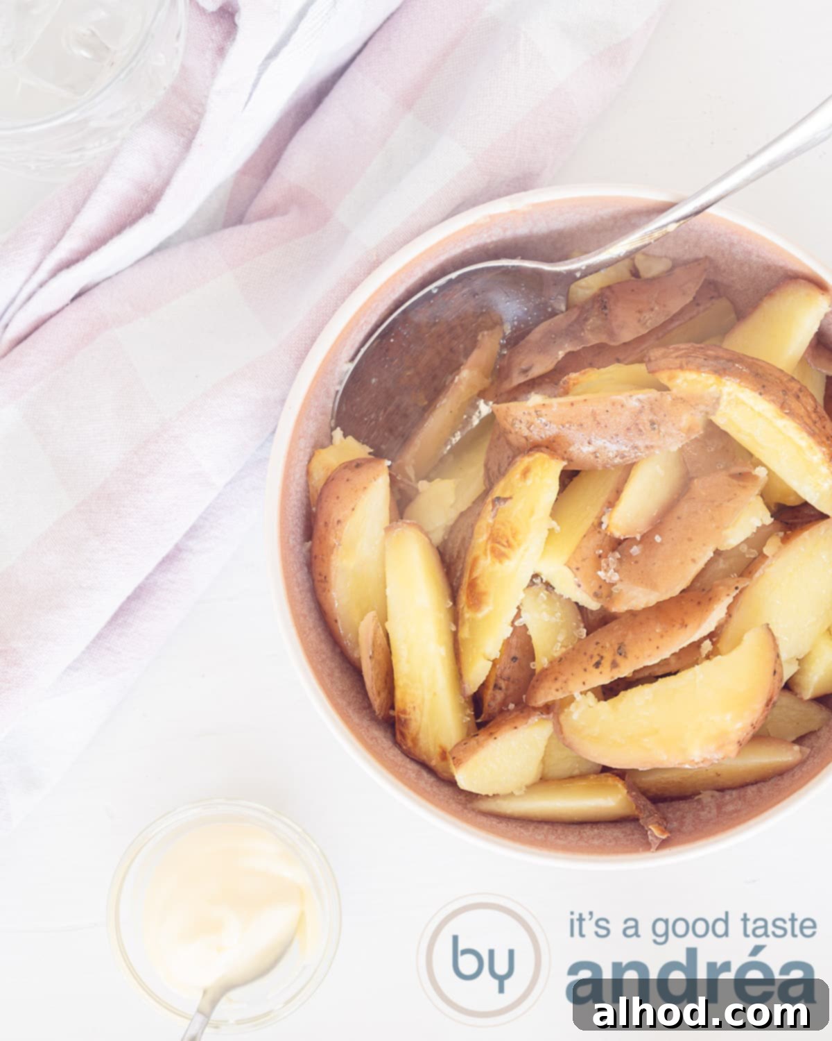 A photo from above with a pink bowl filled with thick fries on a white background in the center left. Top left a pink white tea towel. At the bottom a bowl with mayonnaise