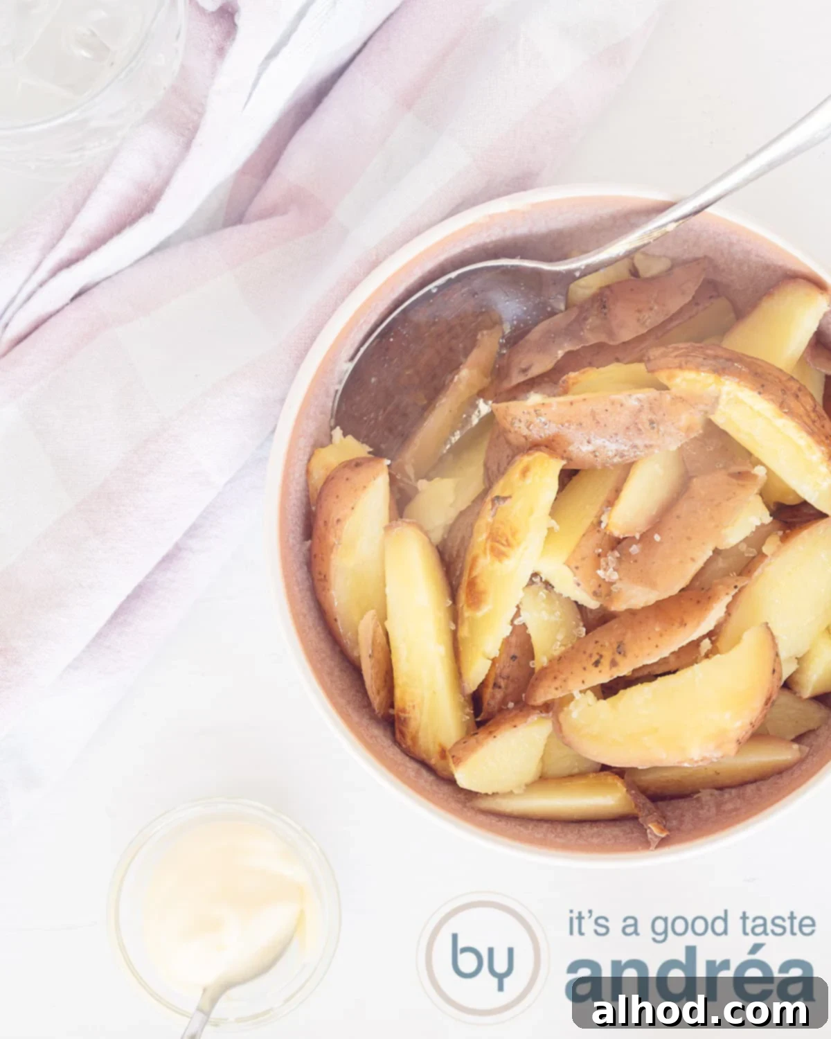 Crispy Oven Fries 2 A photo from above with a pink bowl filled with thick fries on a white background in the center left. Top left a pink white tea towel. At the bottom a bowl with mayonnaise